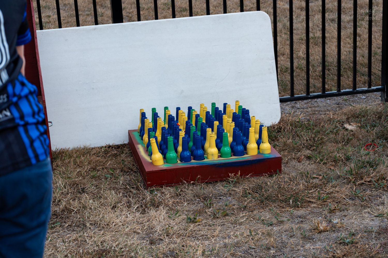 Colorful blue and yellow chess pieces on a wooden board set on grass outdoors near a fence.