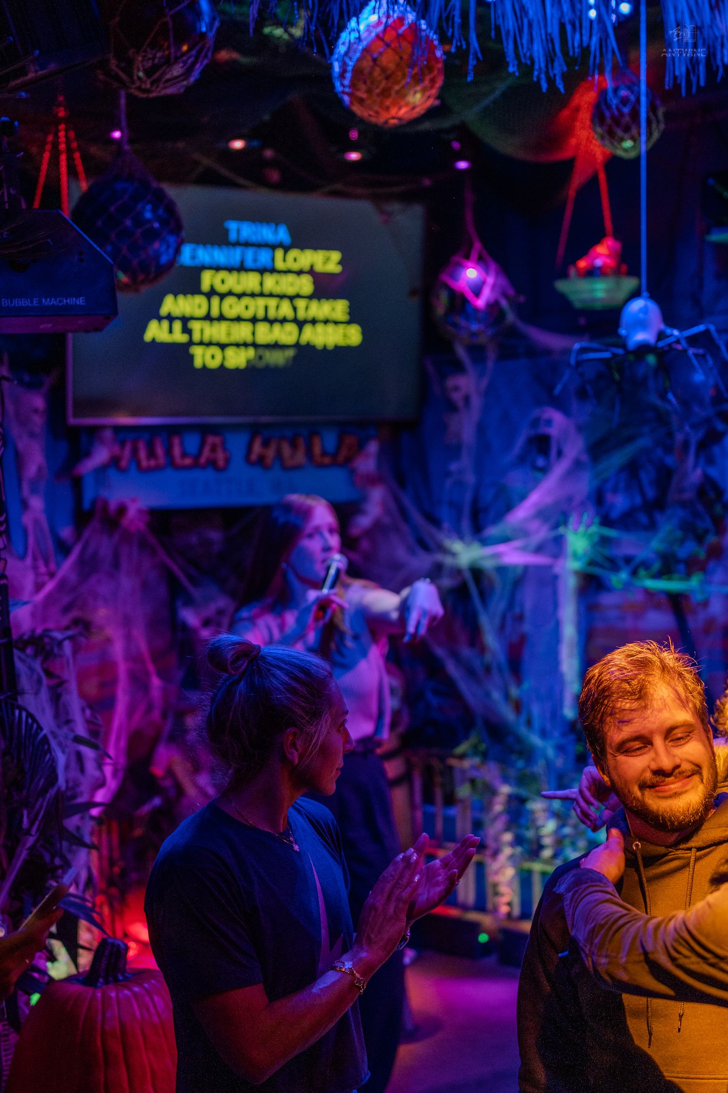 People enjoying Halloween karaoke night at a spooky decorated bar with colorful lights.