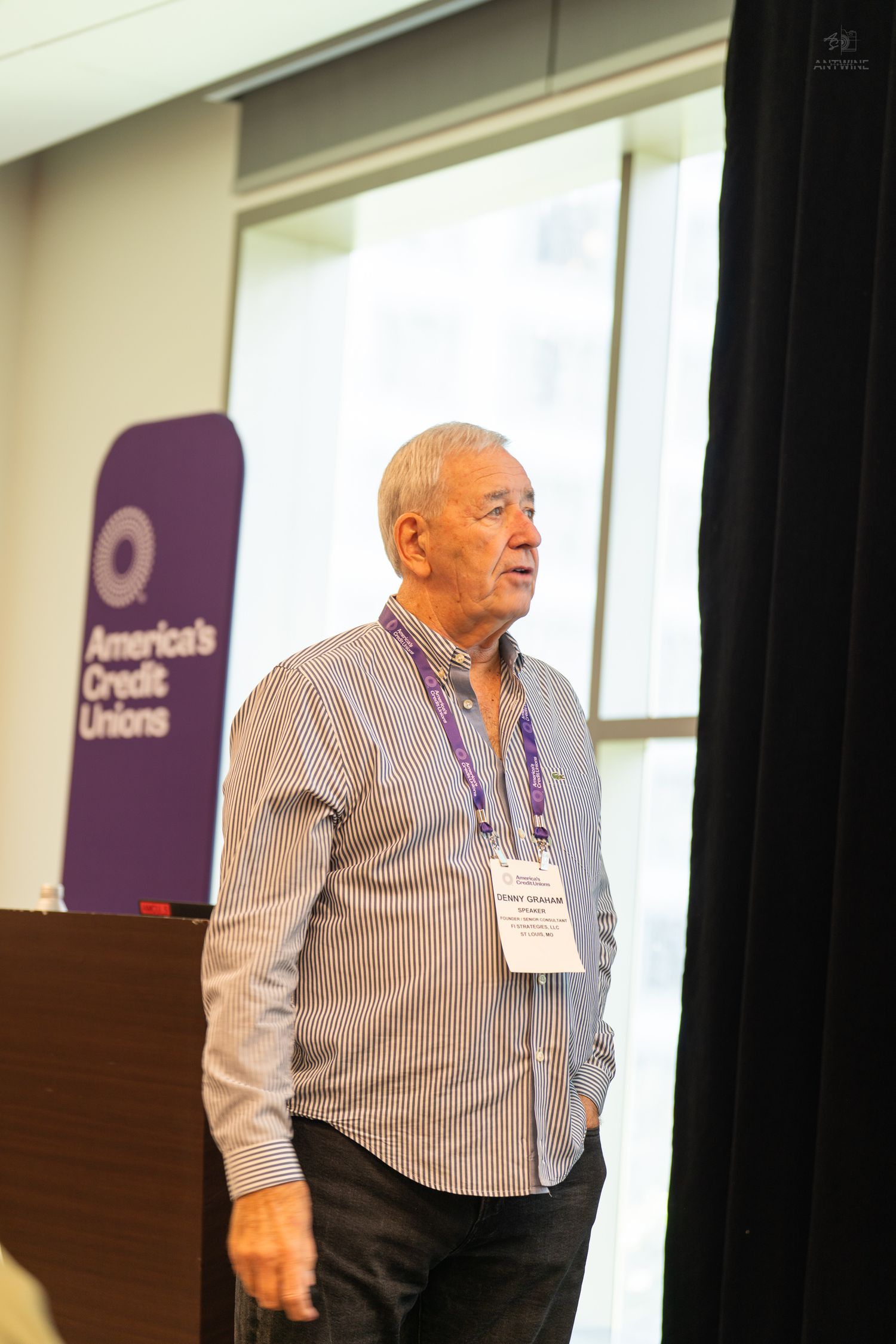 Senior man presenting at America's Credit Unions conference wearing badge and striped shirt.