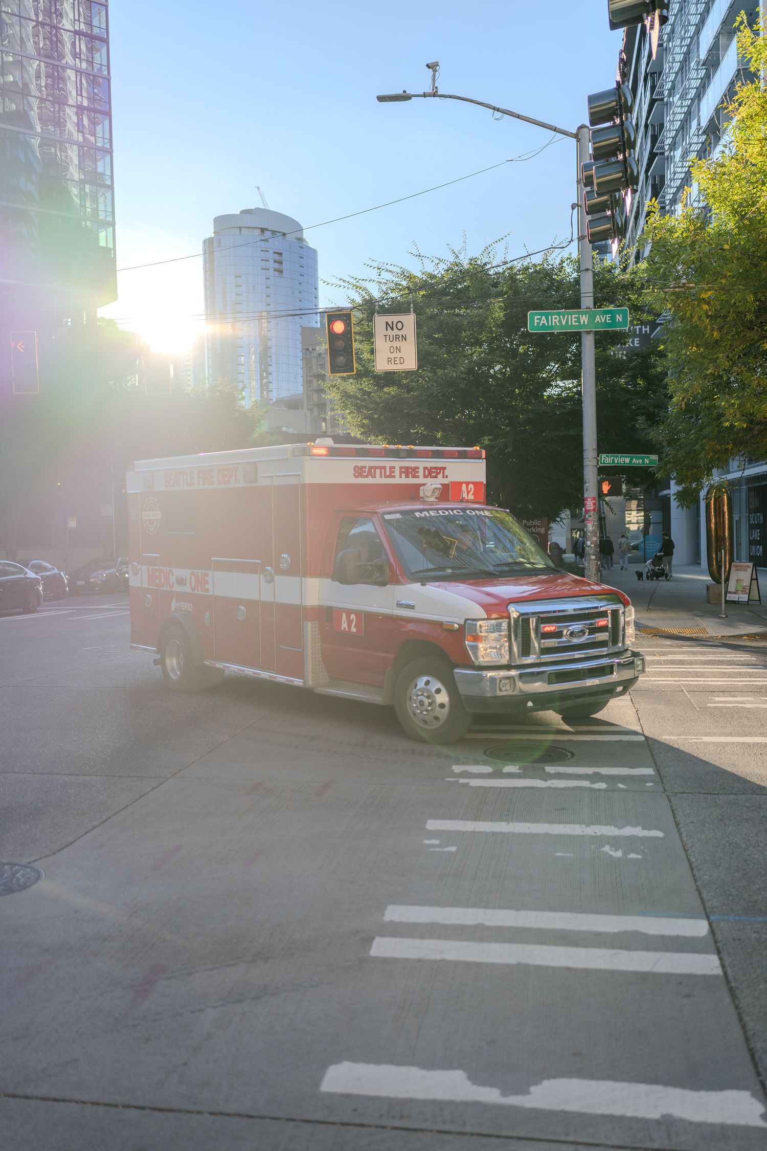 Seattle Fire Dept red ambulance at a sunny urban intersection near Fairview Ave, city buildings in background.