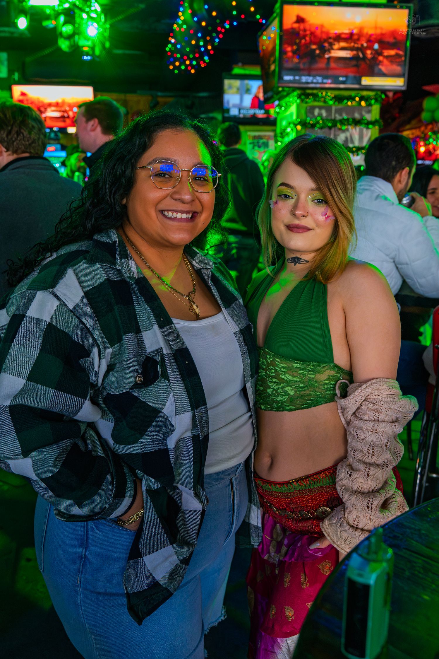 Two women smiling together at a St. Patrick's Day bar celebration with green lighting.