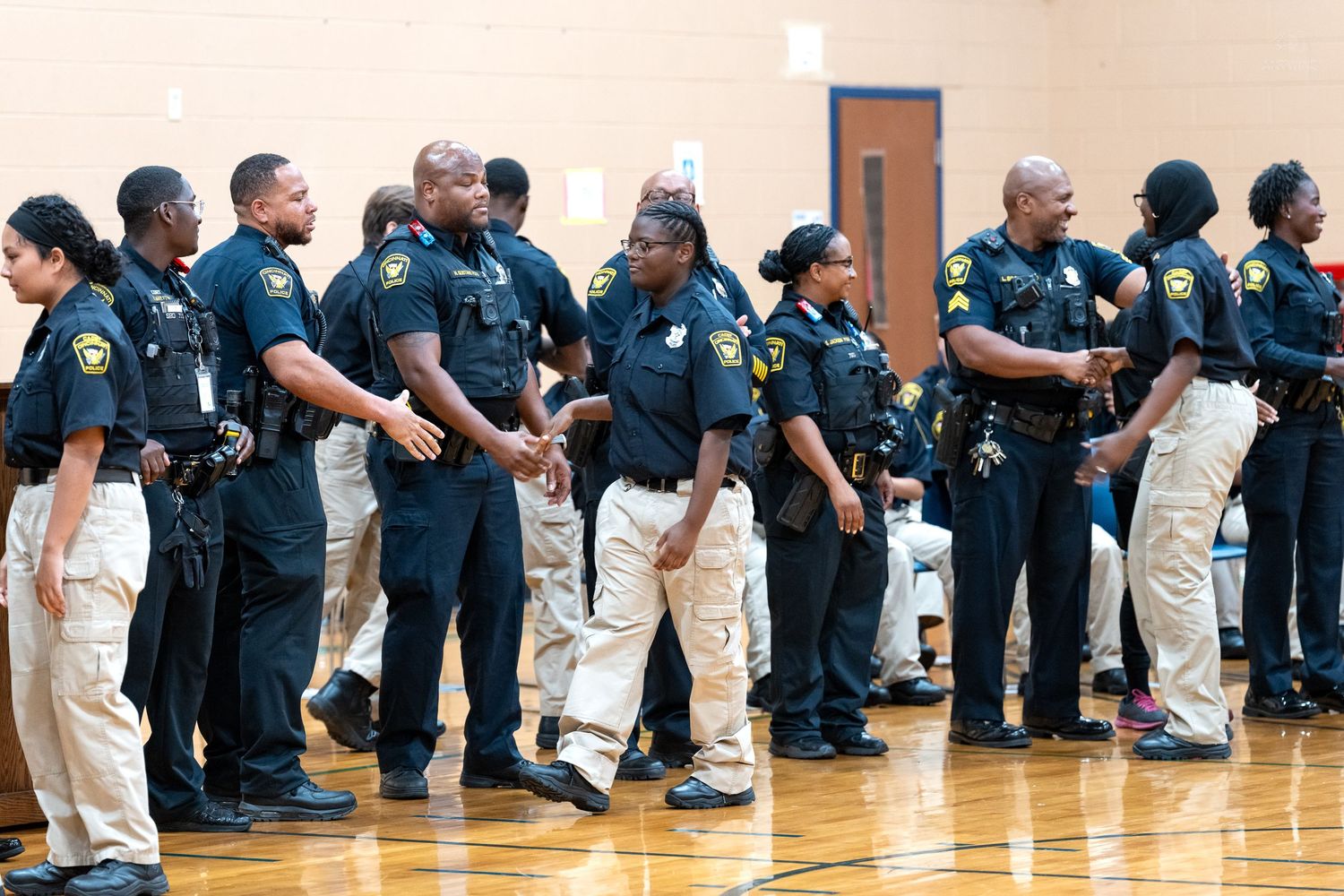 Group of law enforcement officers in uniform standing in a gymnasium during a training or briefing event.