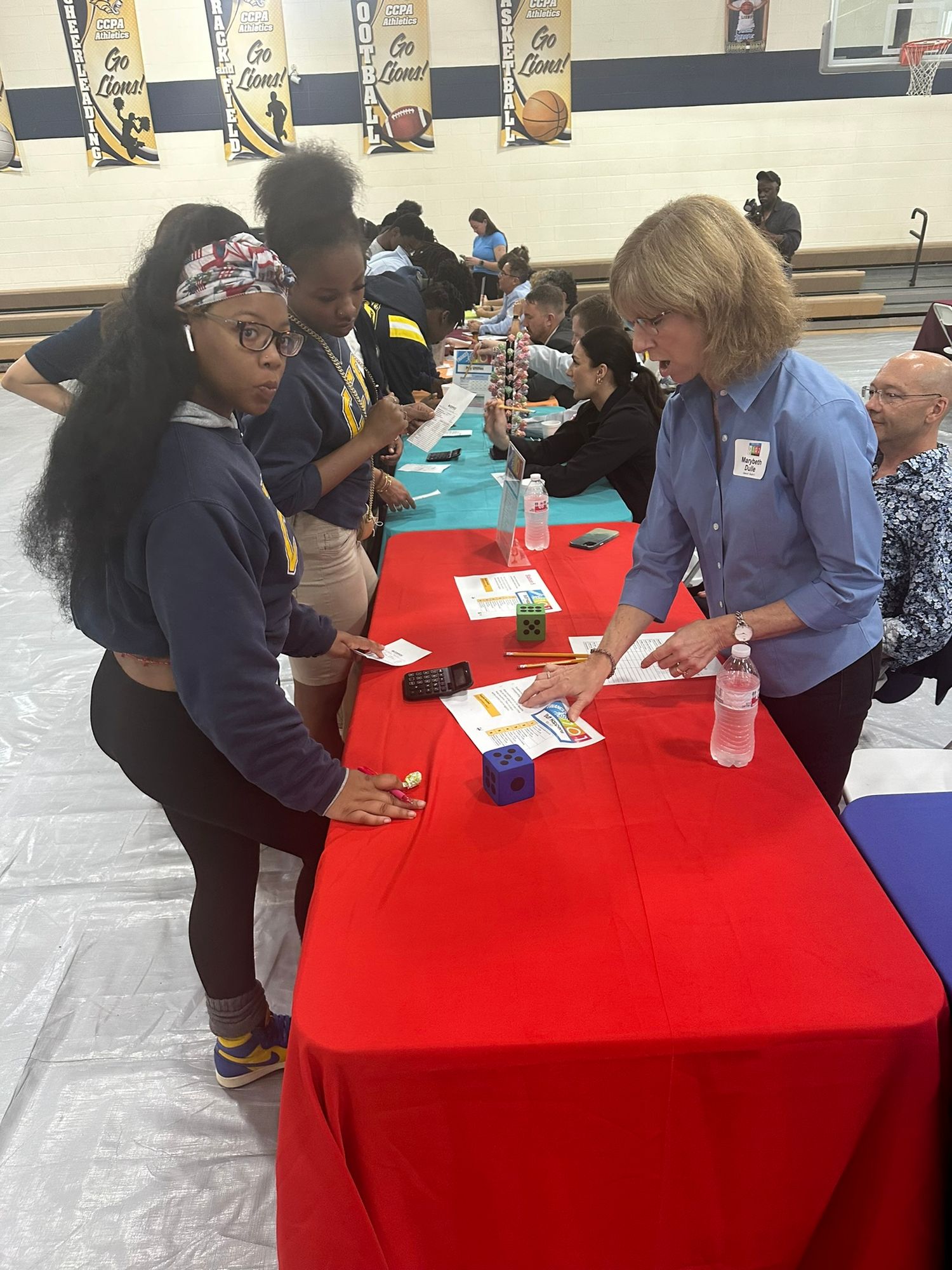 Students interact with a recruiter at a red table during a school career fair held in a gymnasium.