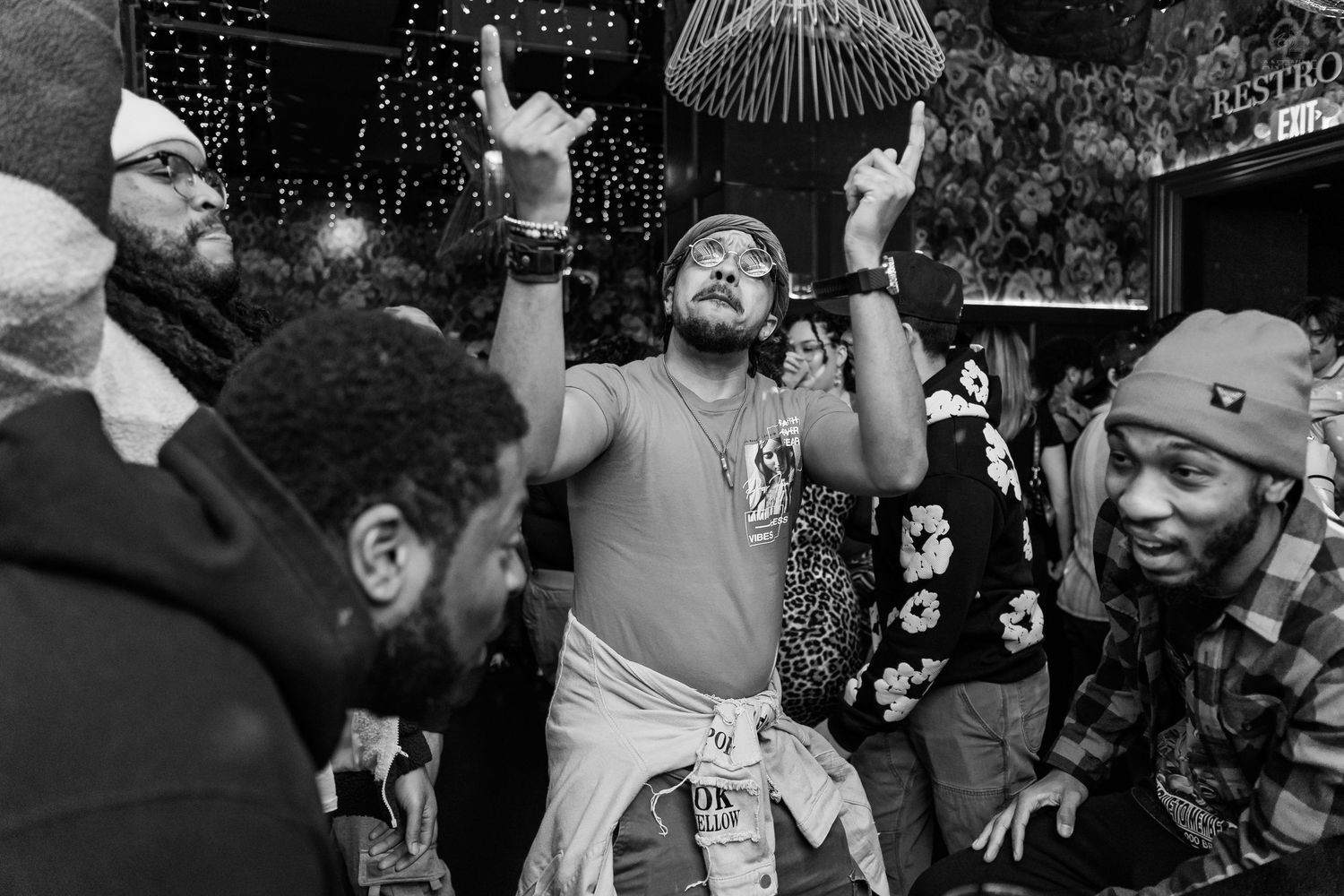 Man dancing enthusiastically with hands raised at a crowded nightclub party in black and white.