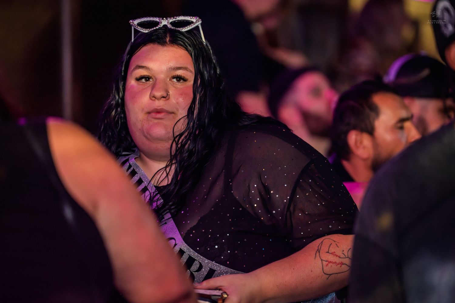 Woman in black mesh top with sunglasses on head at a crowded outdoor event.