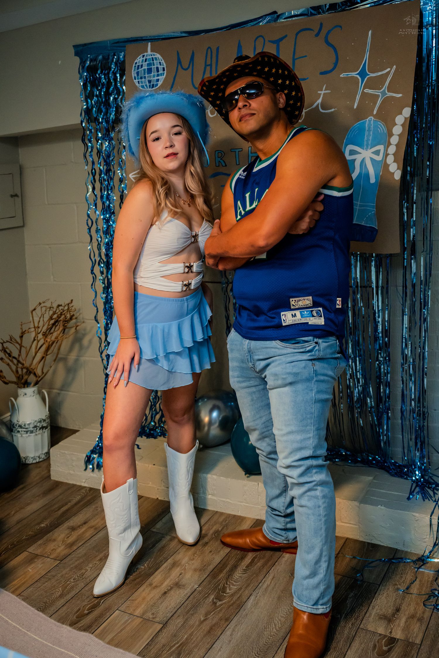 A young woman in blue cowboy hat and mini skirt poses with a man in Dallas jersey at a birthday party.