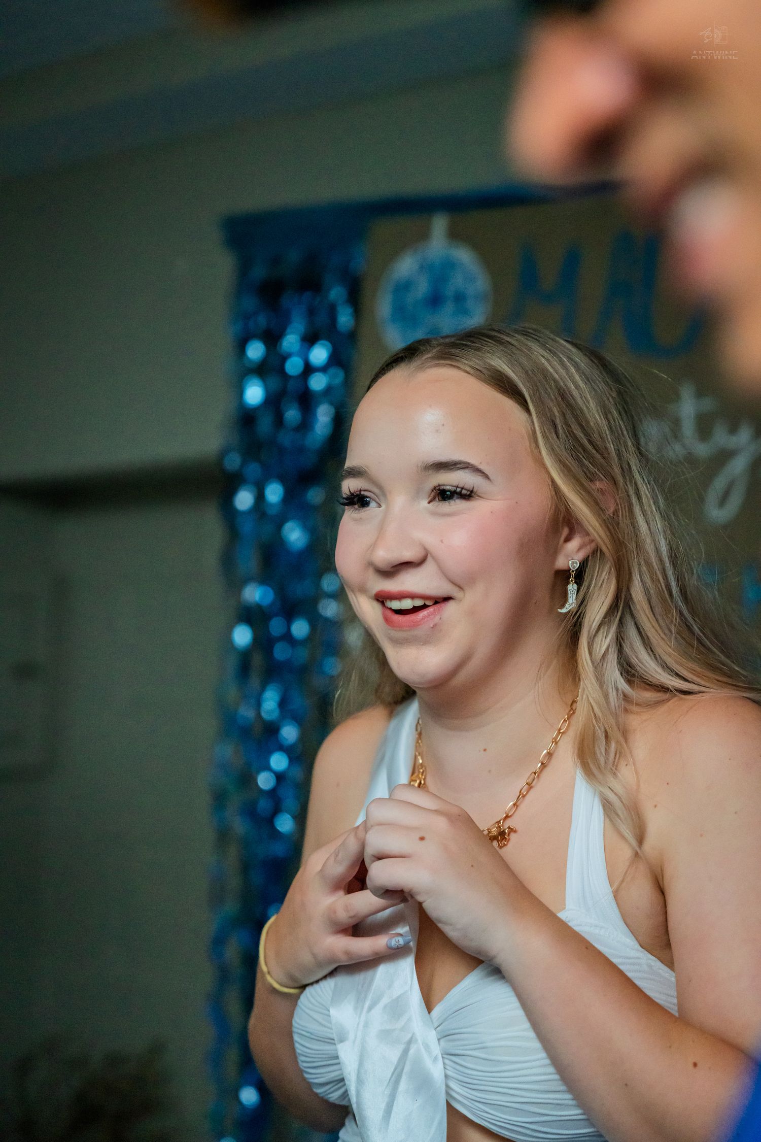 Smiling blonde woman in white halter top with gold chain necklace at a birthday celebration.