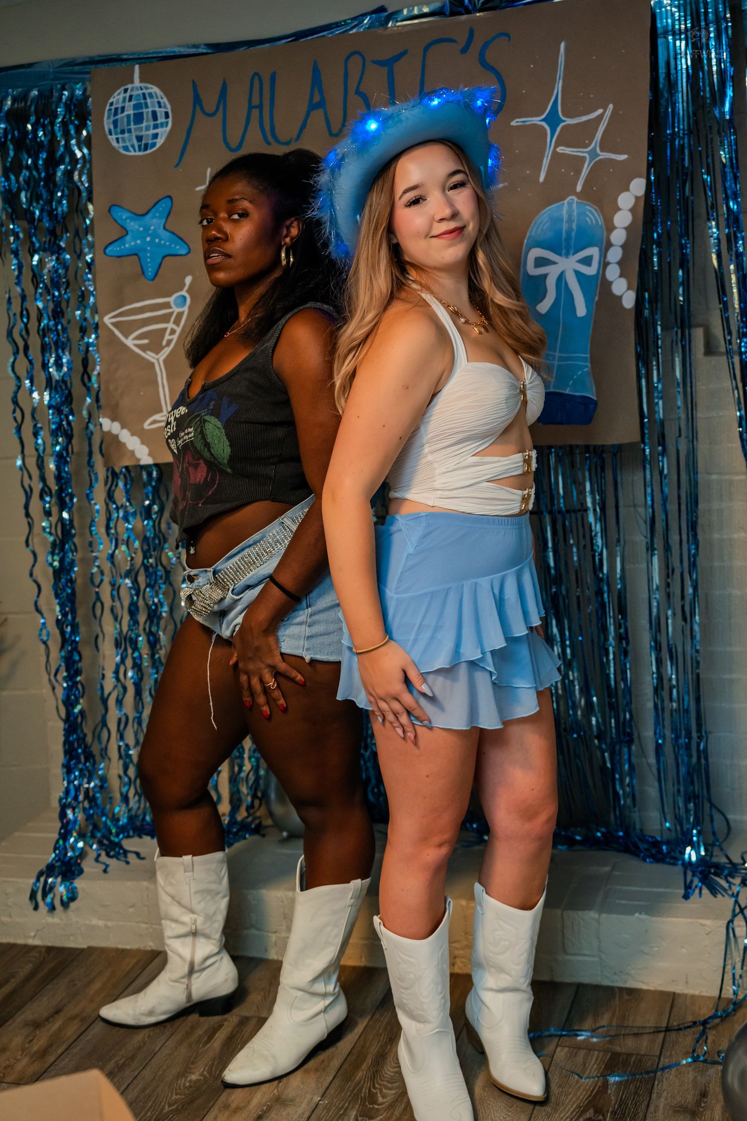 Two young women pose at Malarie's blue-themed party, one wearing a glowing blue LED cowboy hat.