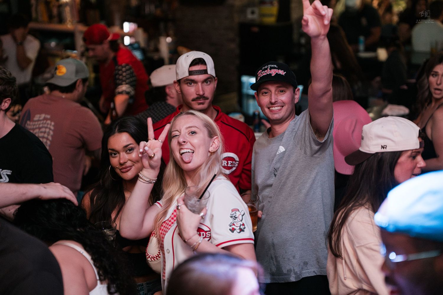 A cheerful group poses with peace signs and raised arms at a Cincinnati bar party.