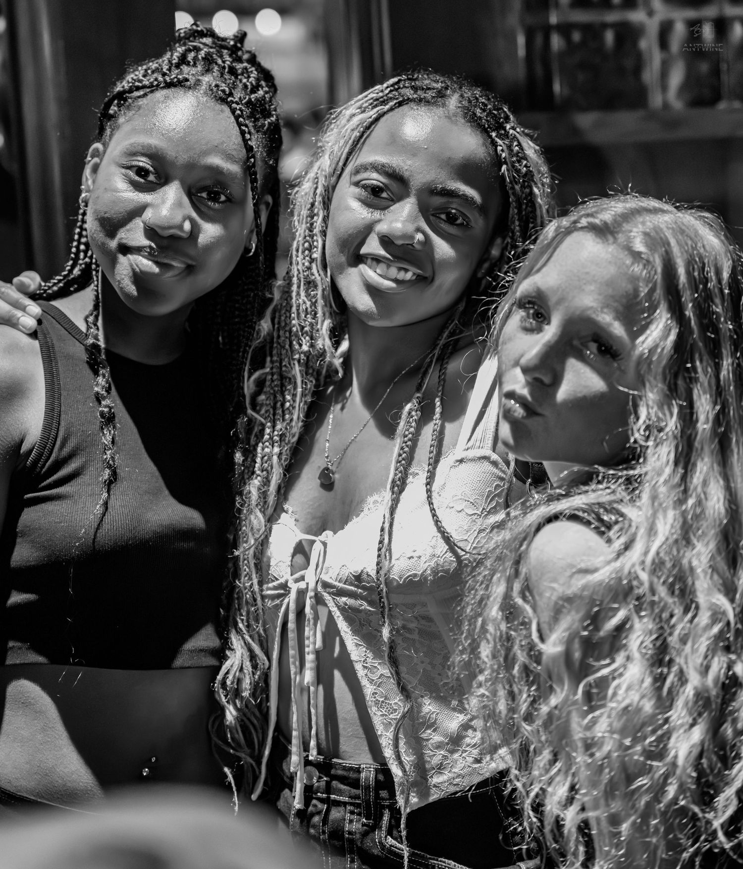 Three young women smiling closely together in a black and white bar photo.