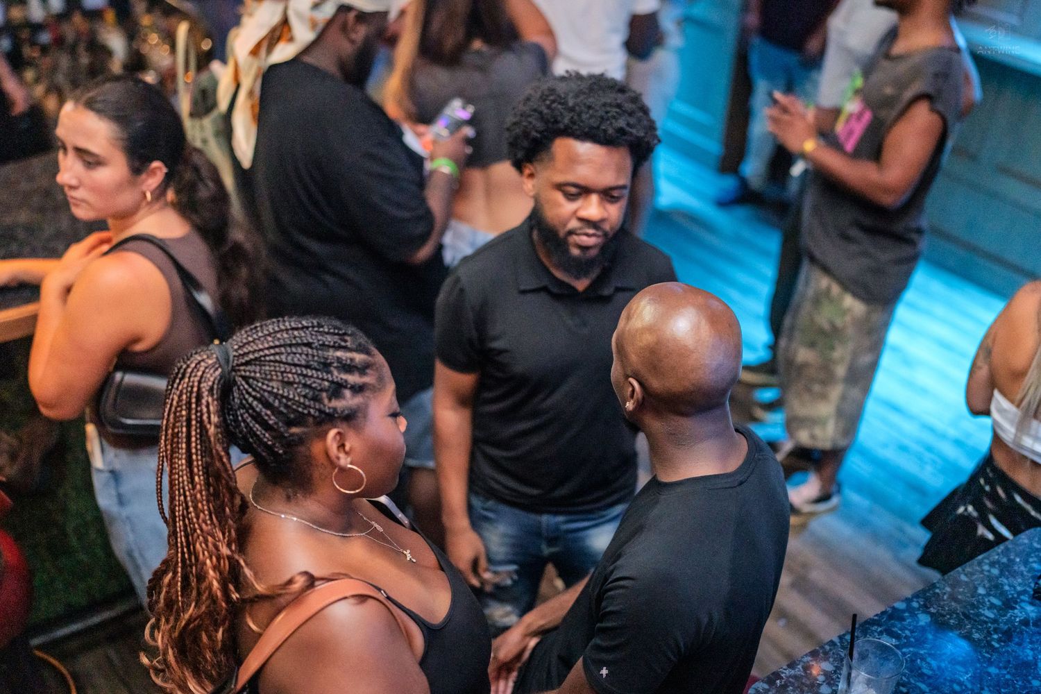 Friends laughing and socializing in a busy nightclub with blue ambient lighting.
