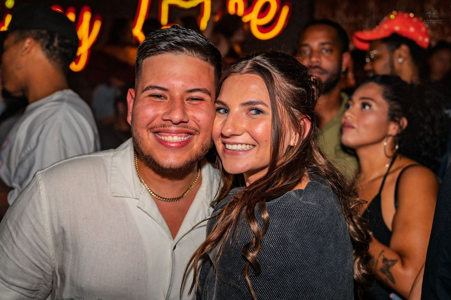 Happy couple smiling at the camera in a crowded nightclub with neon lighting.