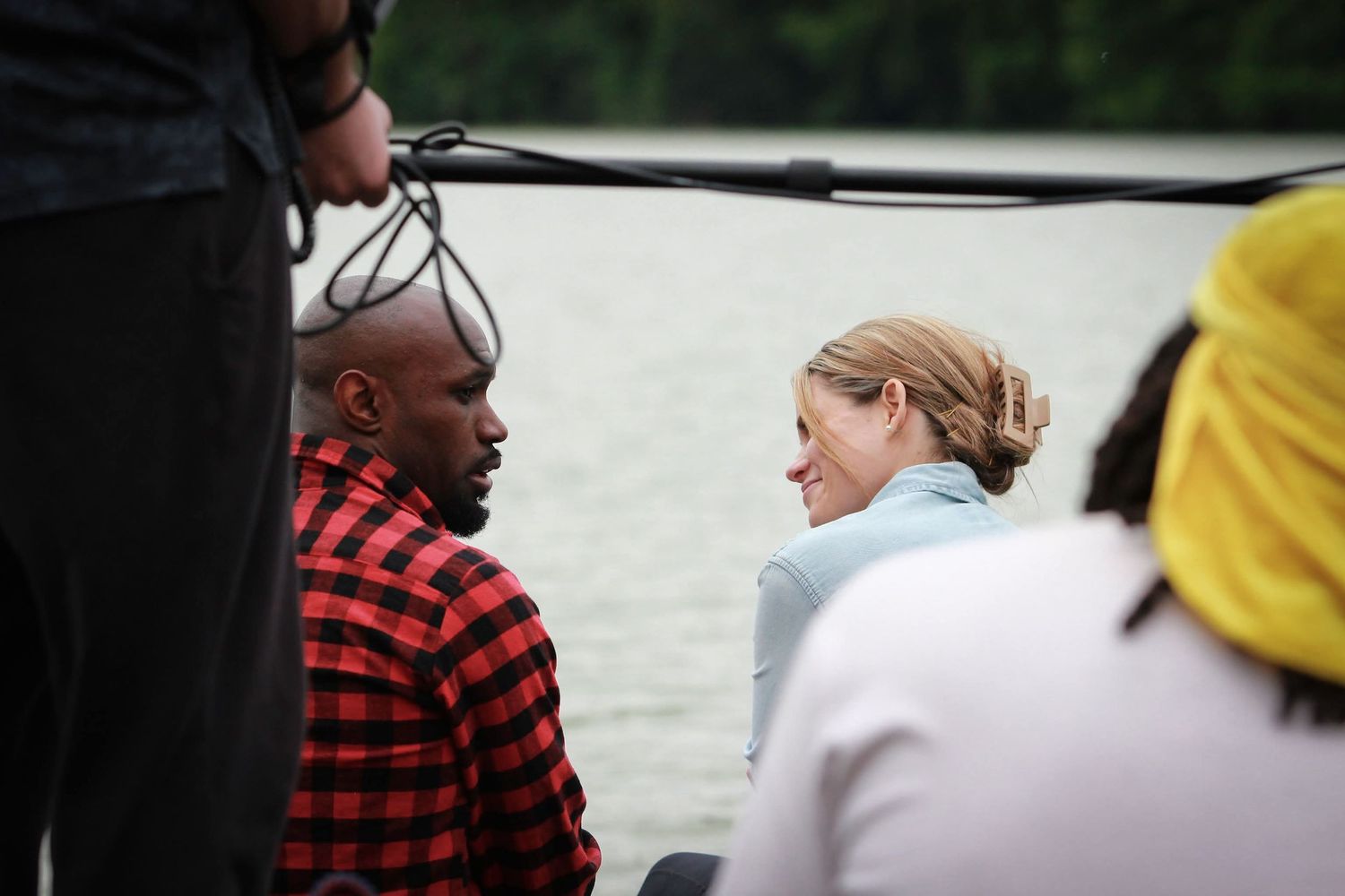 Two people having a conversation on a boat near a calm lake on a cloudy day.