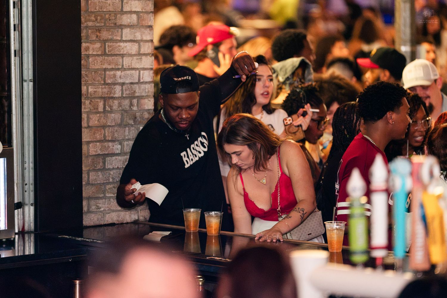 Busy nightclub bar scene with bartender serving drinks to a large crowd of patrons.