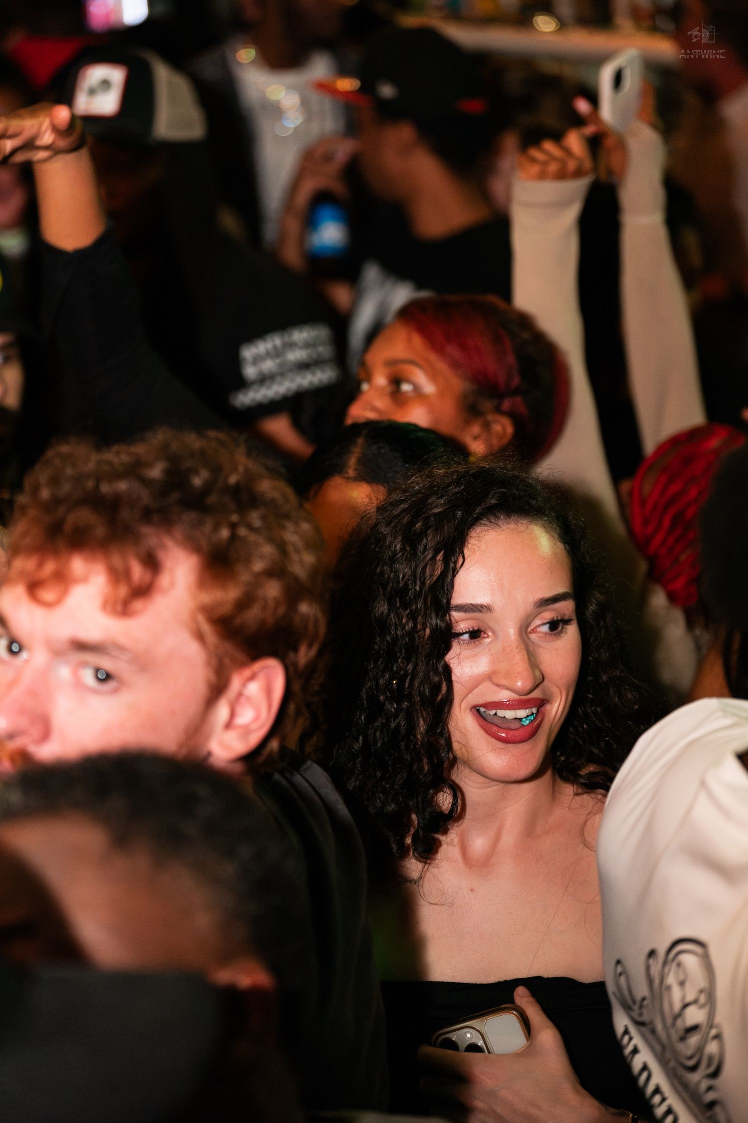 A young woman with curly hair and braces smiles in a dense nighttime crowd.