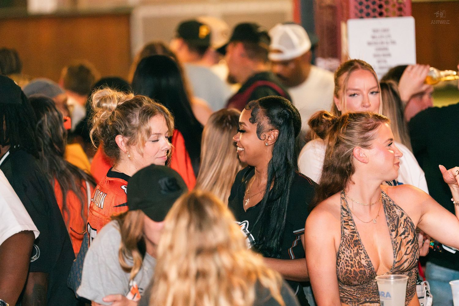Group of women socializing at a crowded indoor party or sports bar event.