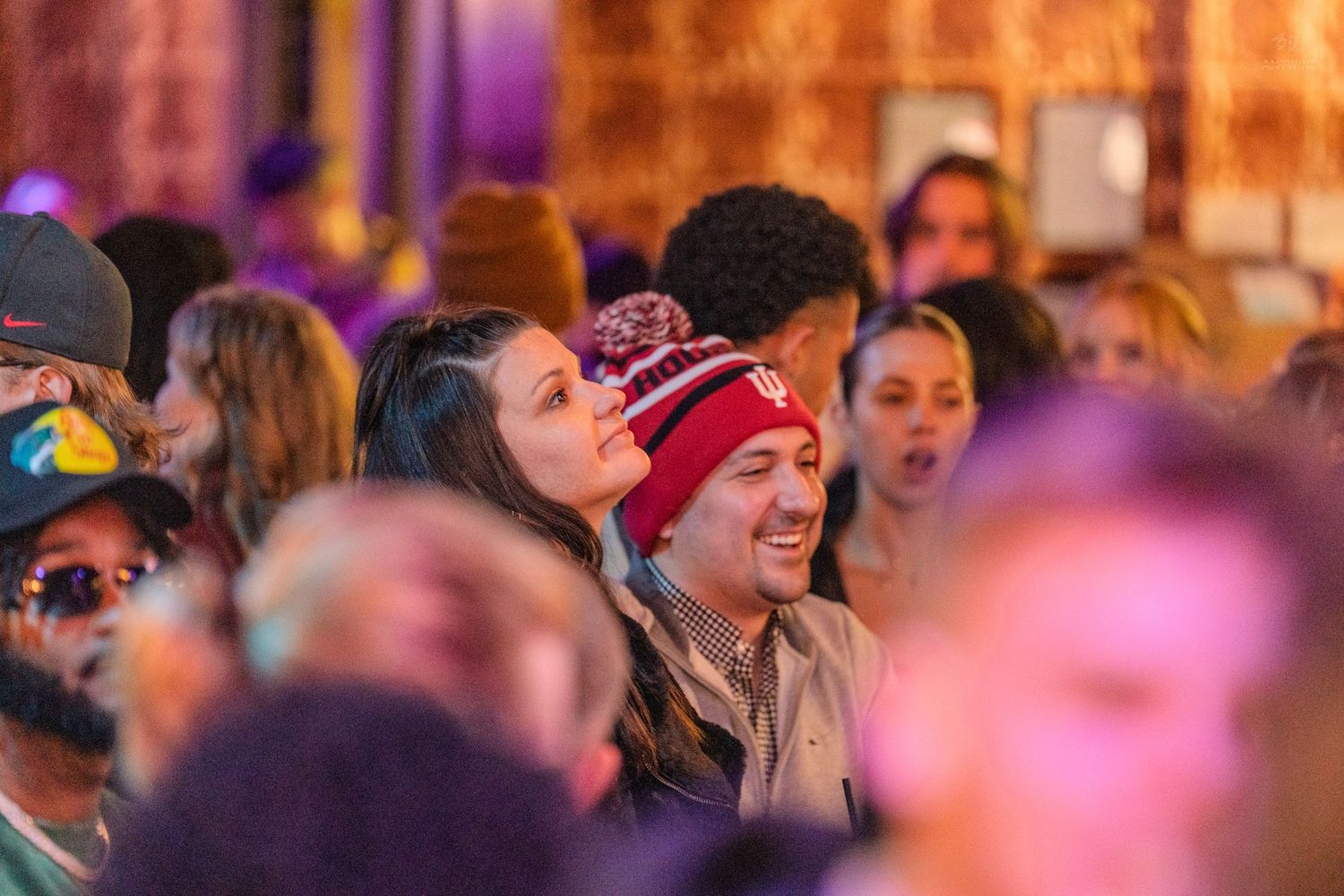 Happy couple smiling and laughing together in a crowded bar, man wearing a red beanie hat.