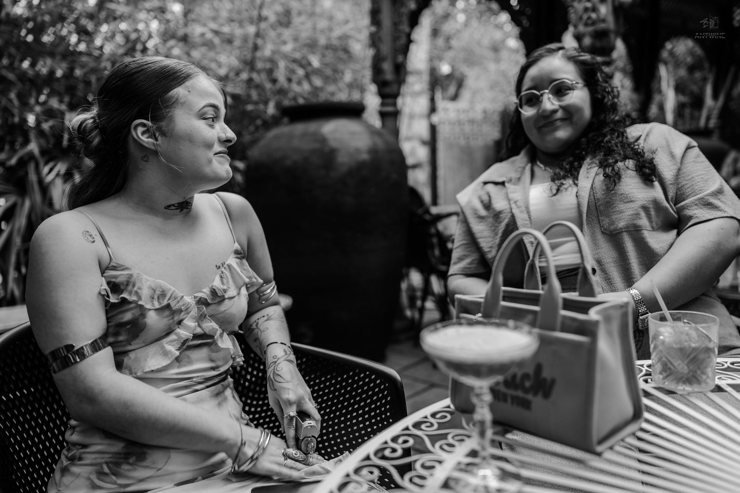 Two women sharing a joyful conversation at outdoor cafe table in black and white photo.