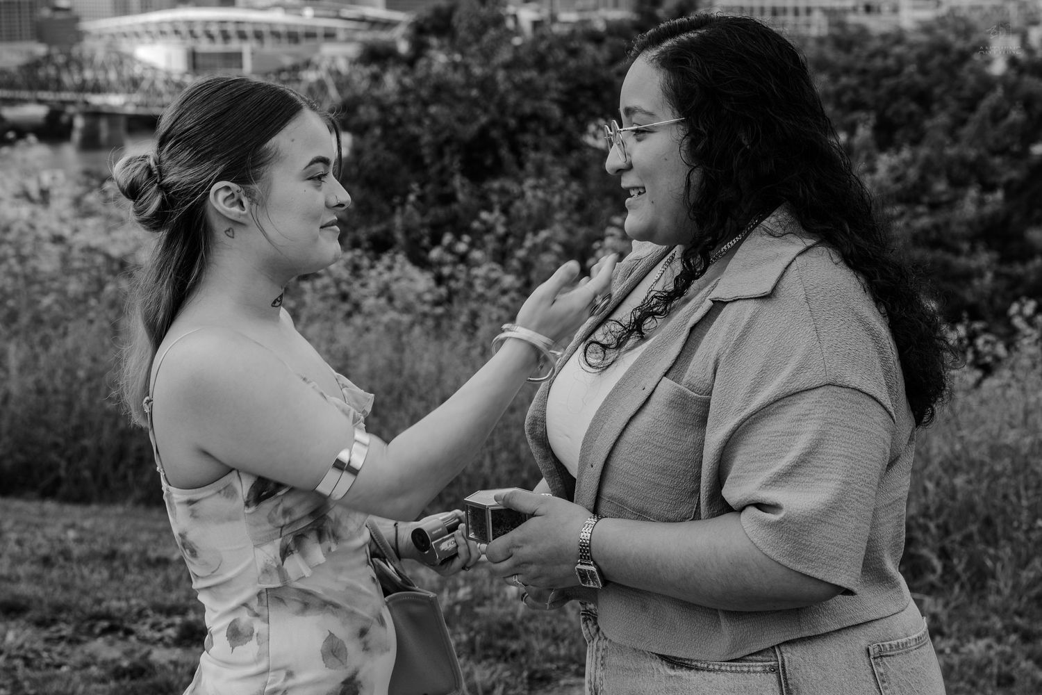 Black and white photo of two women sharing a tender moment outdoors with a city skyline behind them.