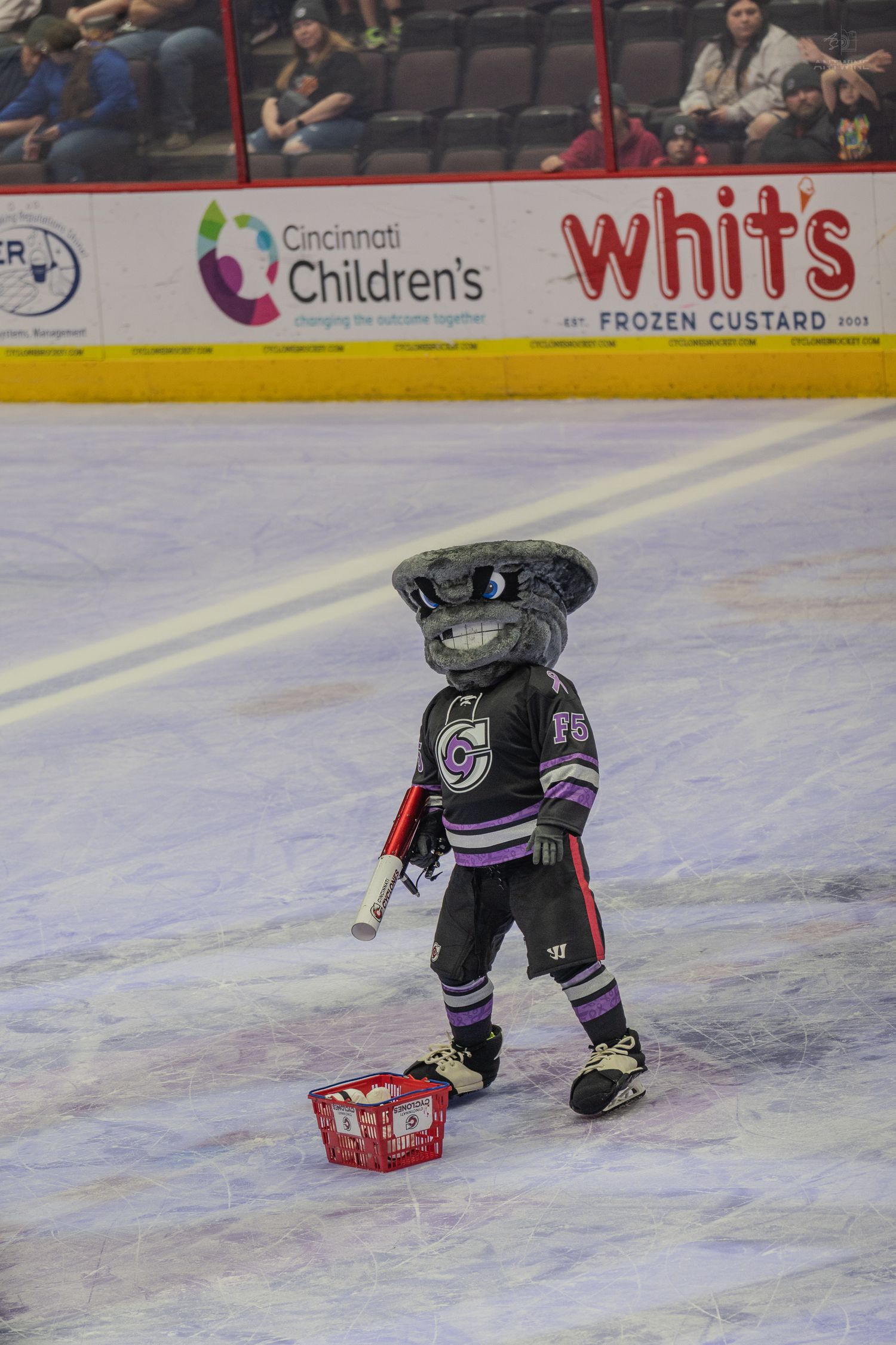 Cincinnati Cyclones hockey mascot skating on ice holding items during a game.