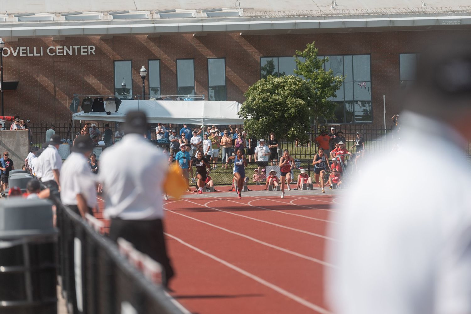 Runners compete on a red track near the Covelli Center during an outdoor track and field event.