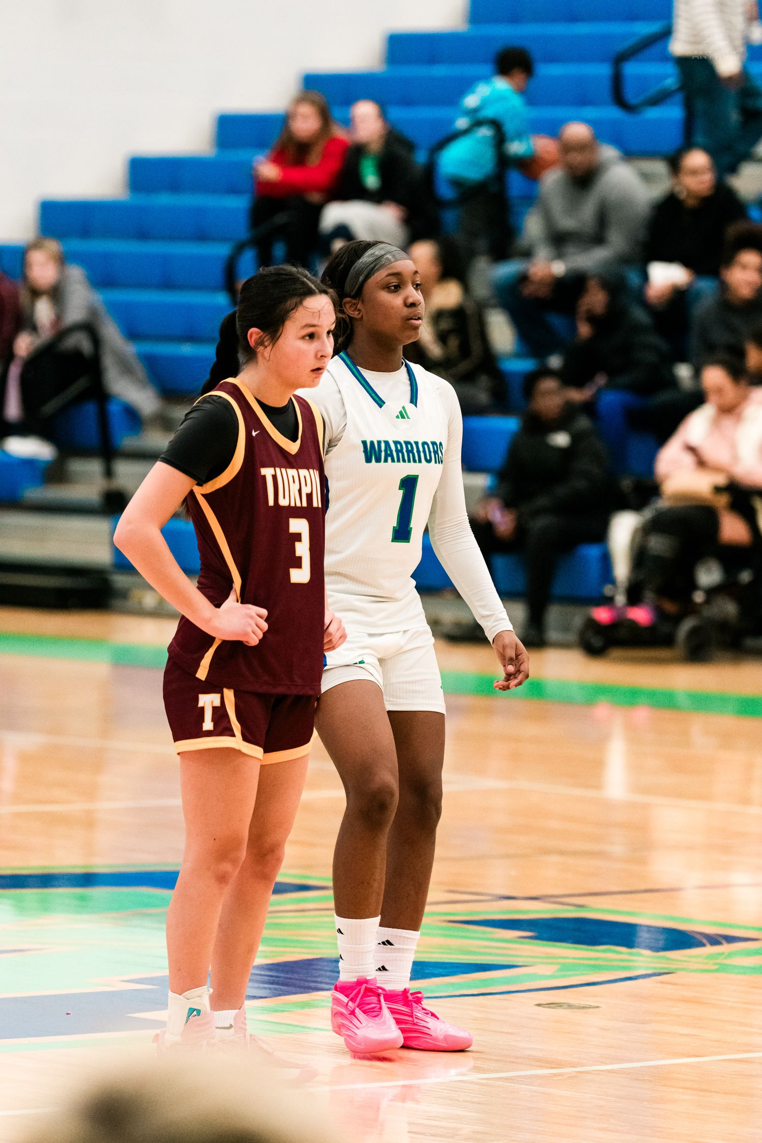 Warriors #1 and Turpin #3 stand side by side awaiting play during girls high school basketball game.