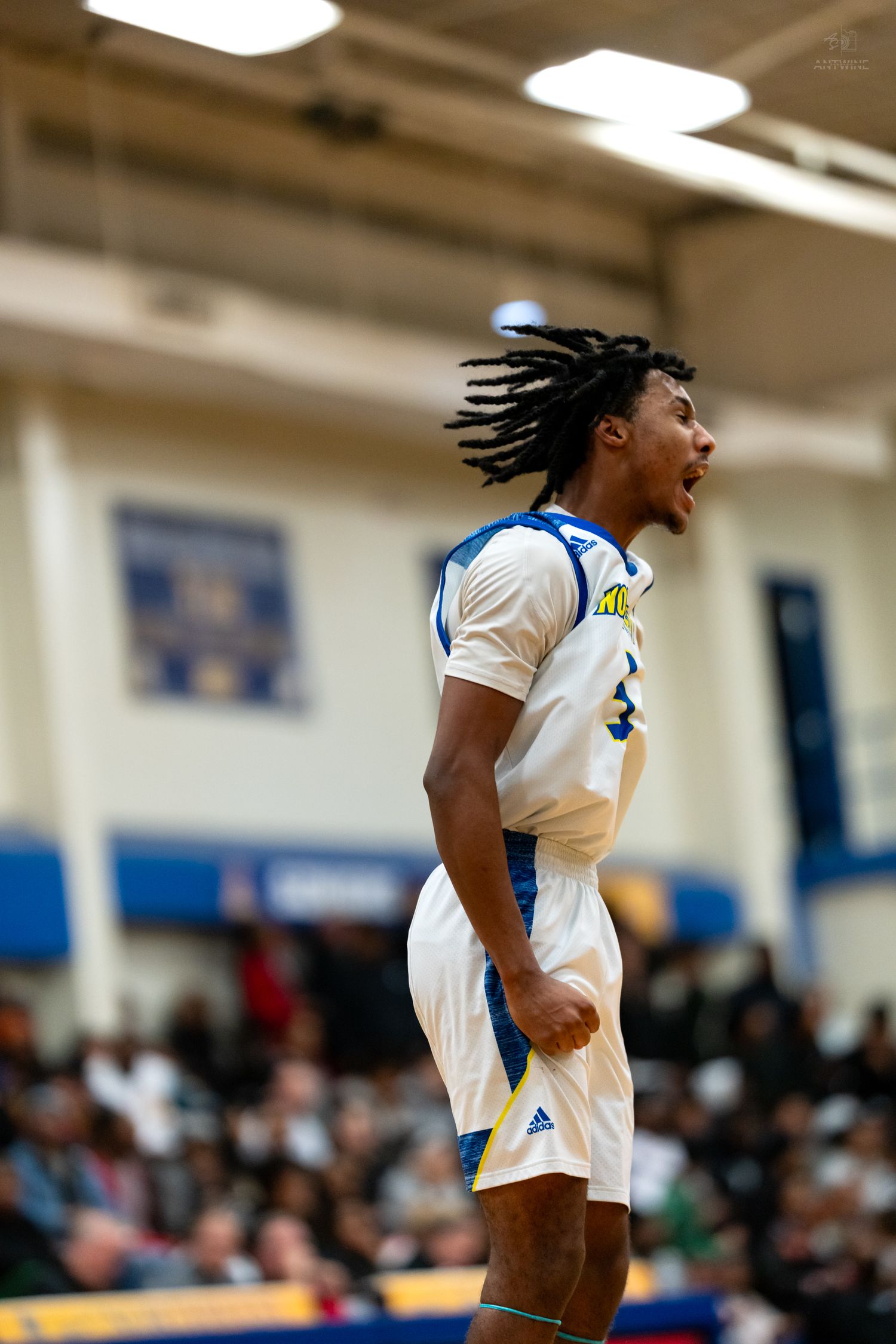 A basketball player in a white and blue uniform celebrates intensely on an indoor court during a game.