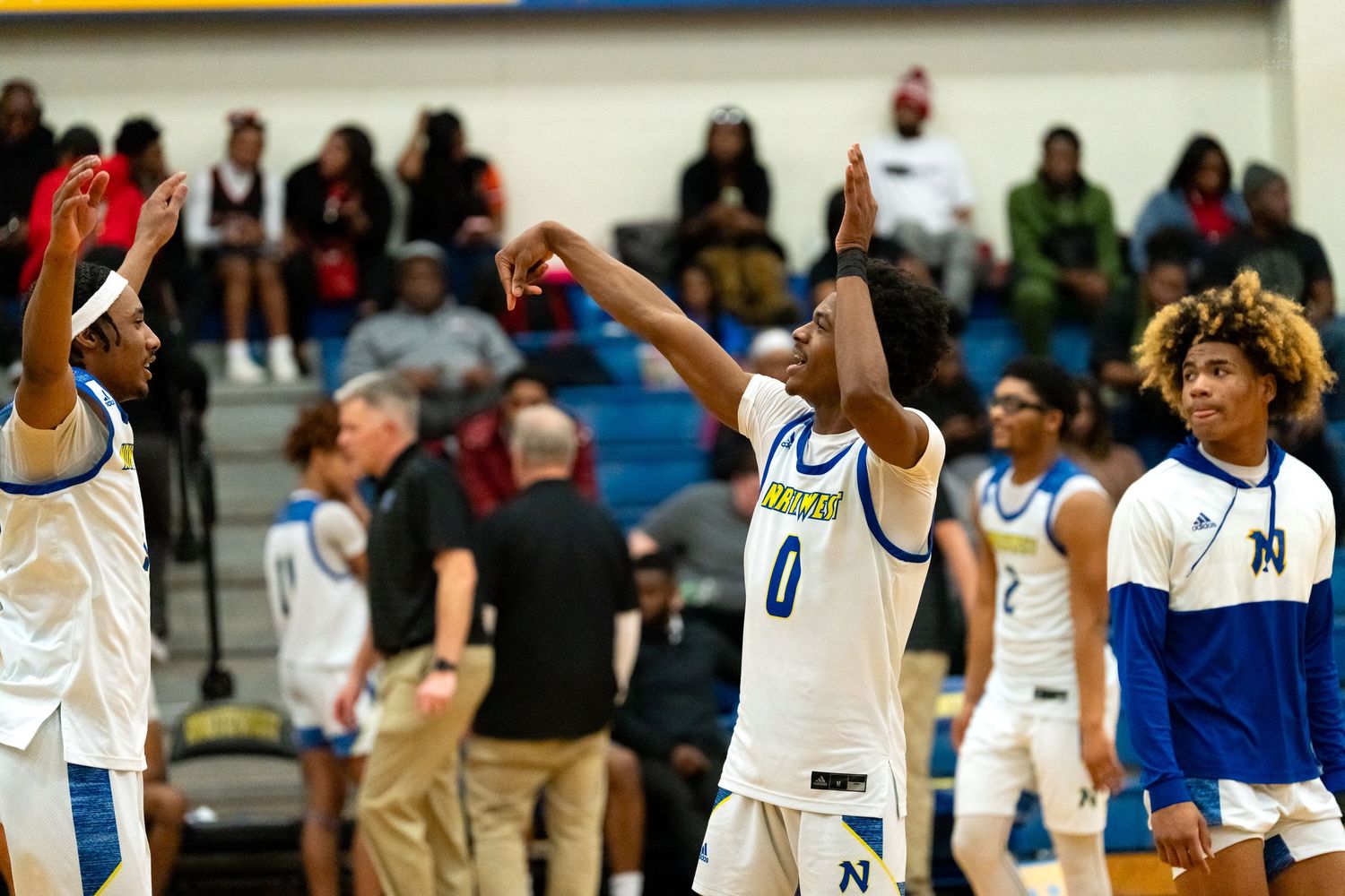 High school basketball players in blue and white uniforms celebrate with raised hands during a home game.