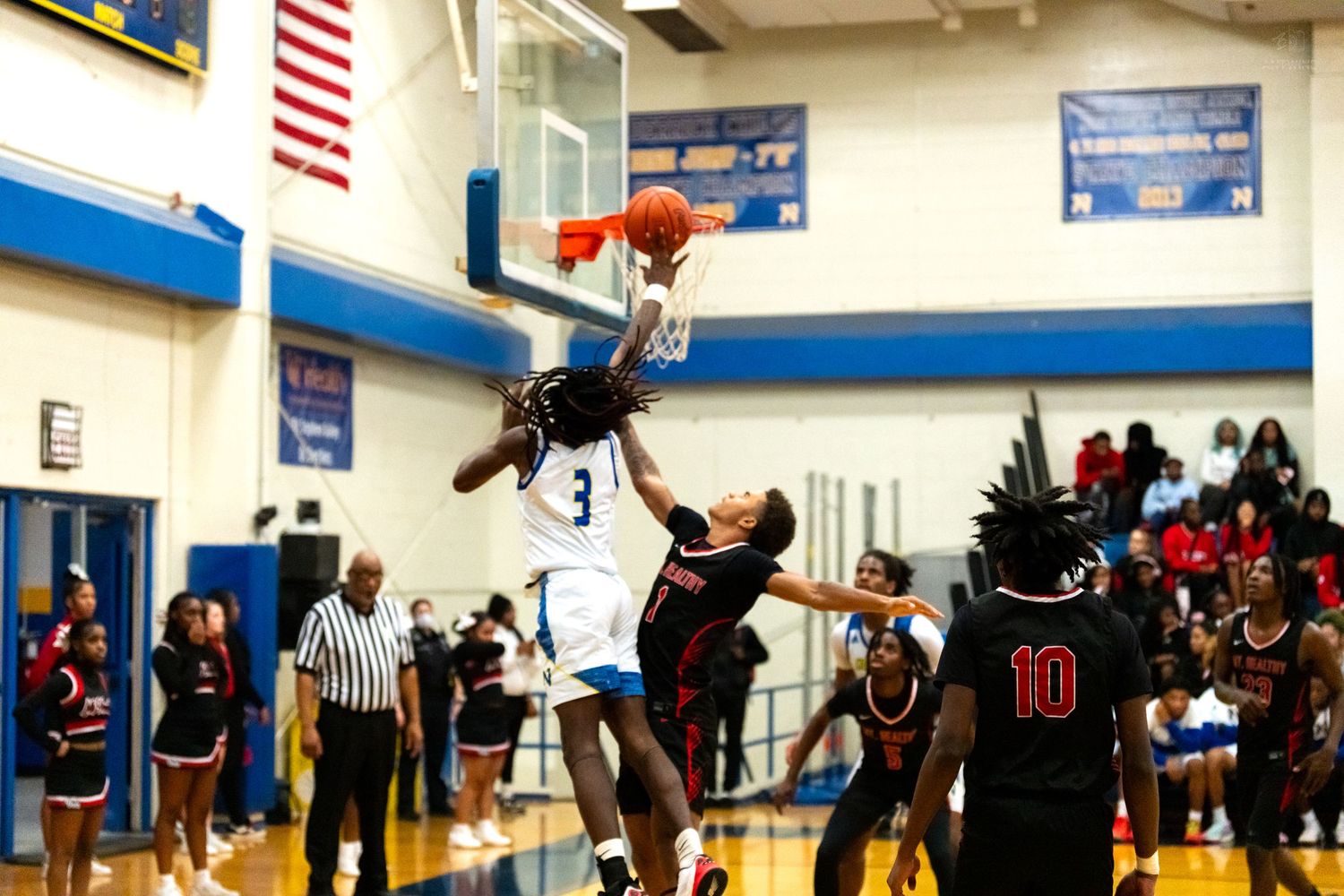 Basketball player number 3 in white attempts layup over defender during high school game in blue and white gym.