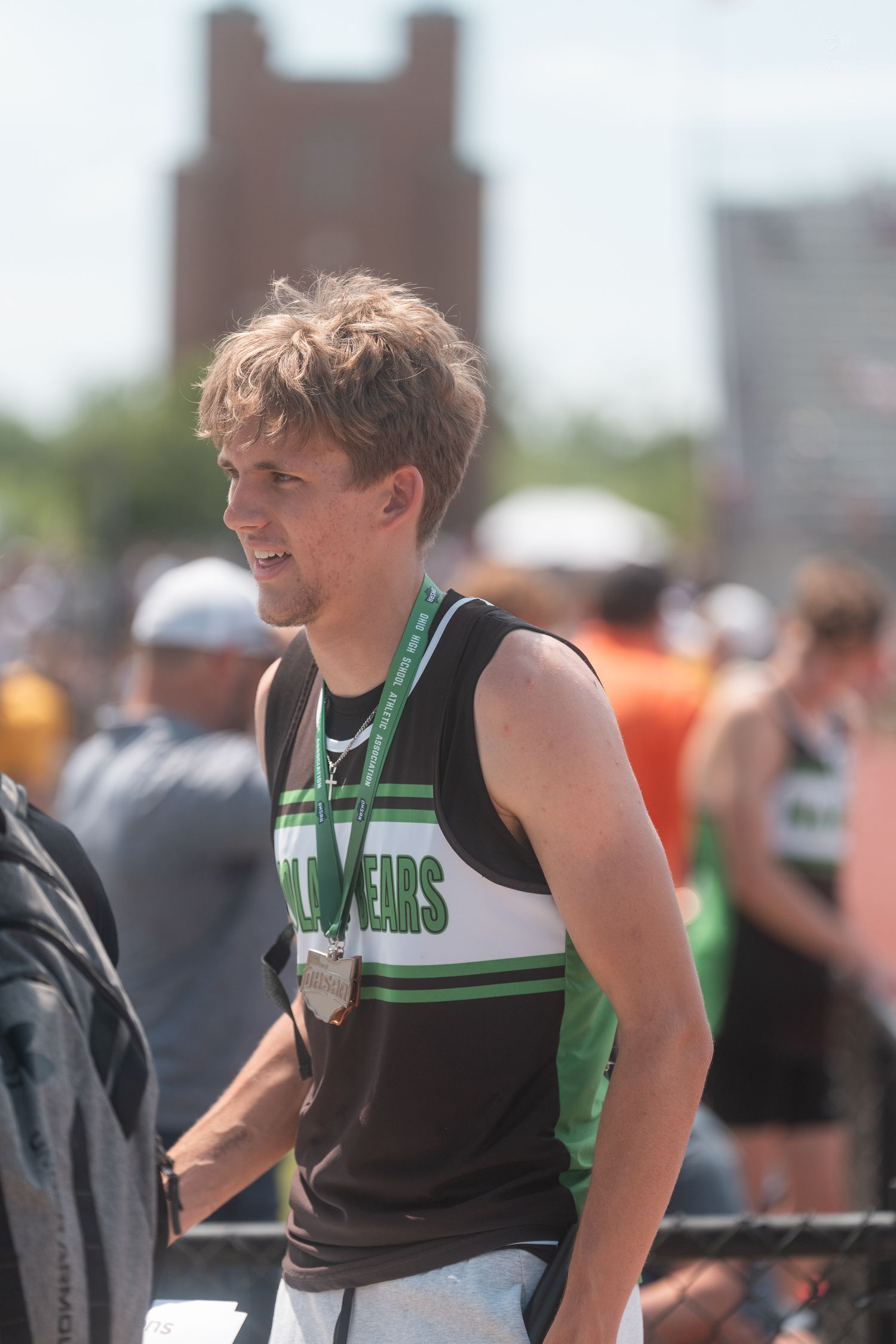 Young male track athlete wearing medal and black green Bears uniform at outdoor competition.