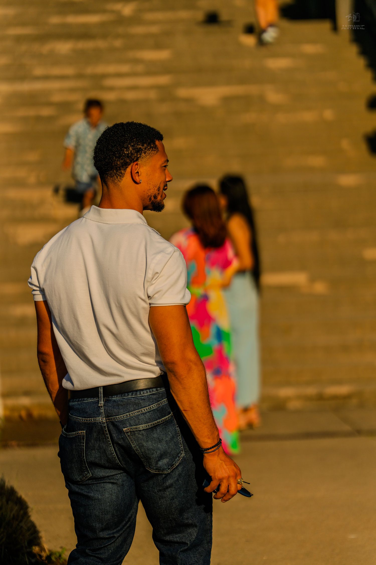 Man in a white t-shirt and jeans looking back over his shoulder on a sunny stairway.