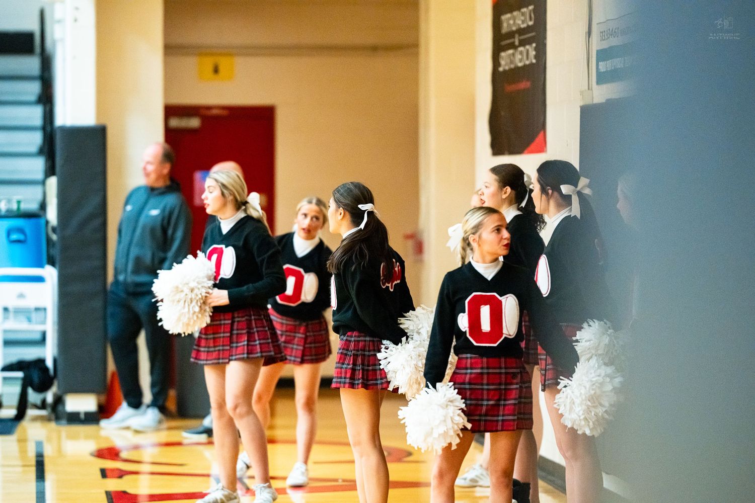 Cheerleaders in red and black uniforms hold white pom-poms during a high school basketball game.