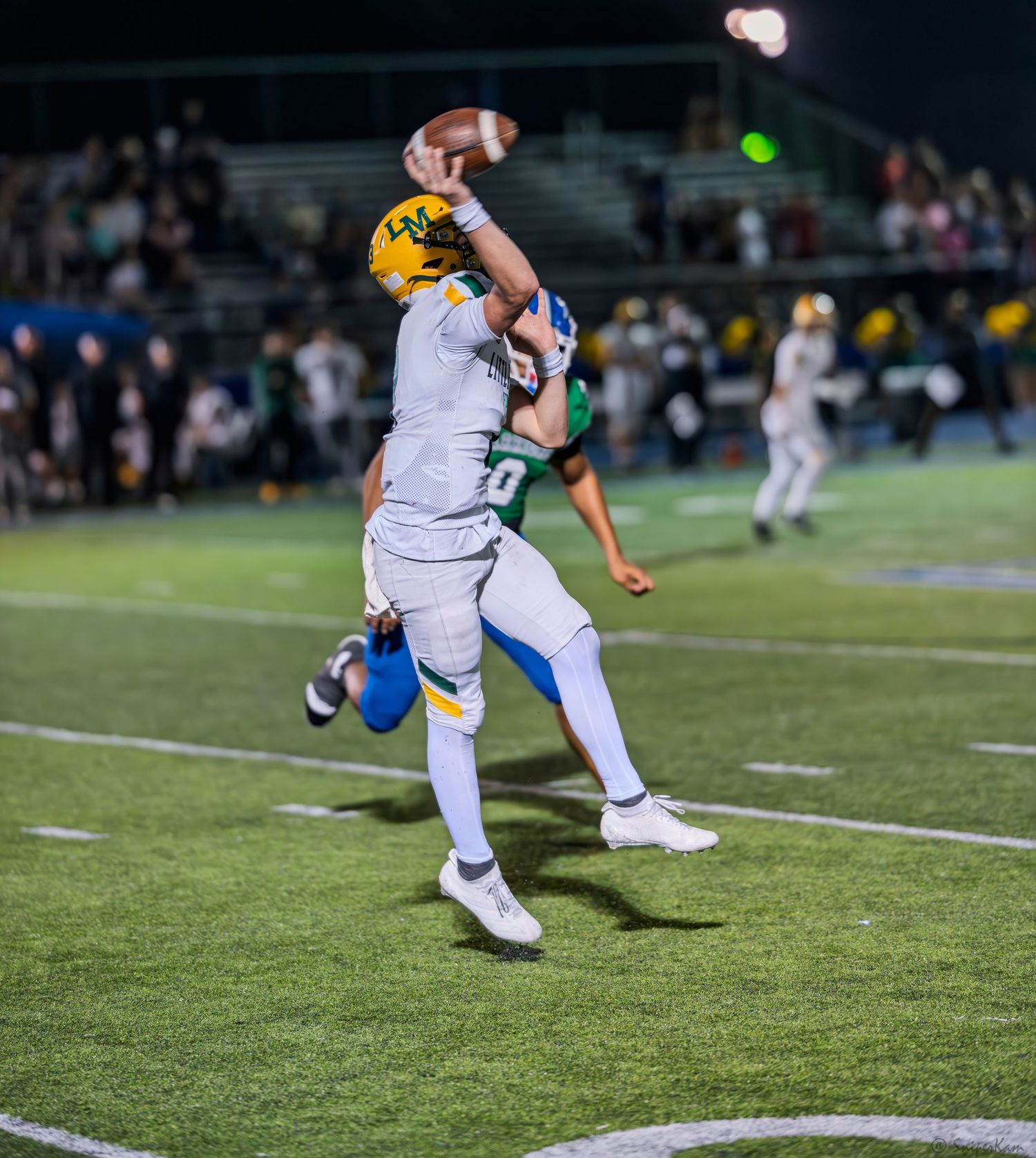 A football player in gold and white uniform leaps to catch a pass near the sideline during a night game.
