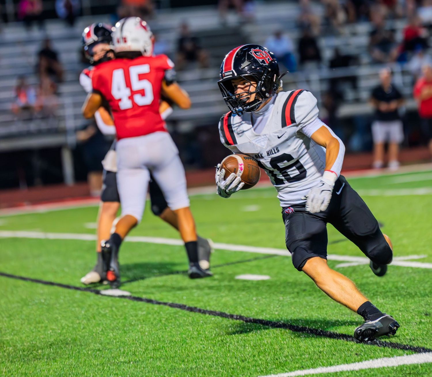 High school football player in black and white uniform runs with the ball during a night game.