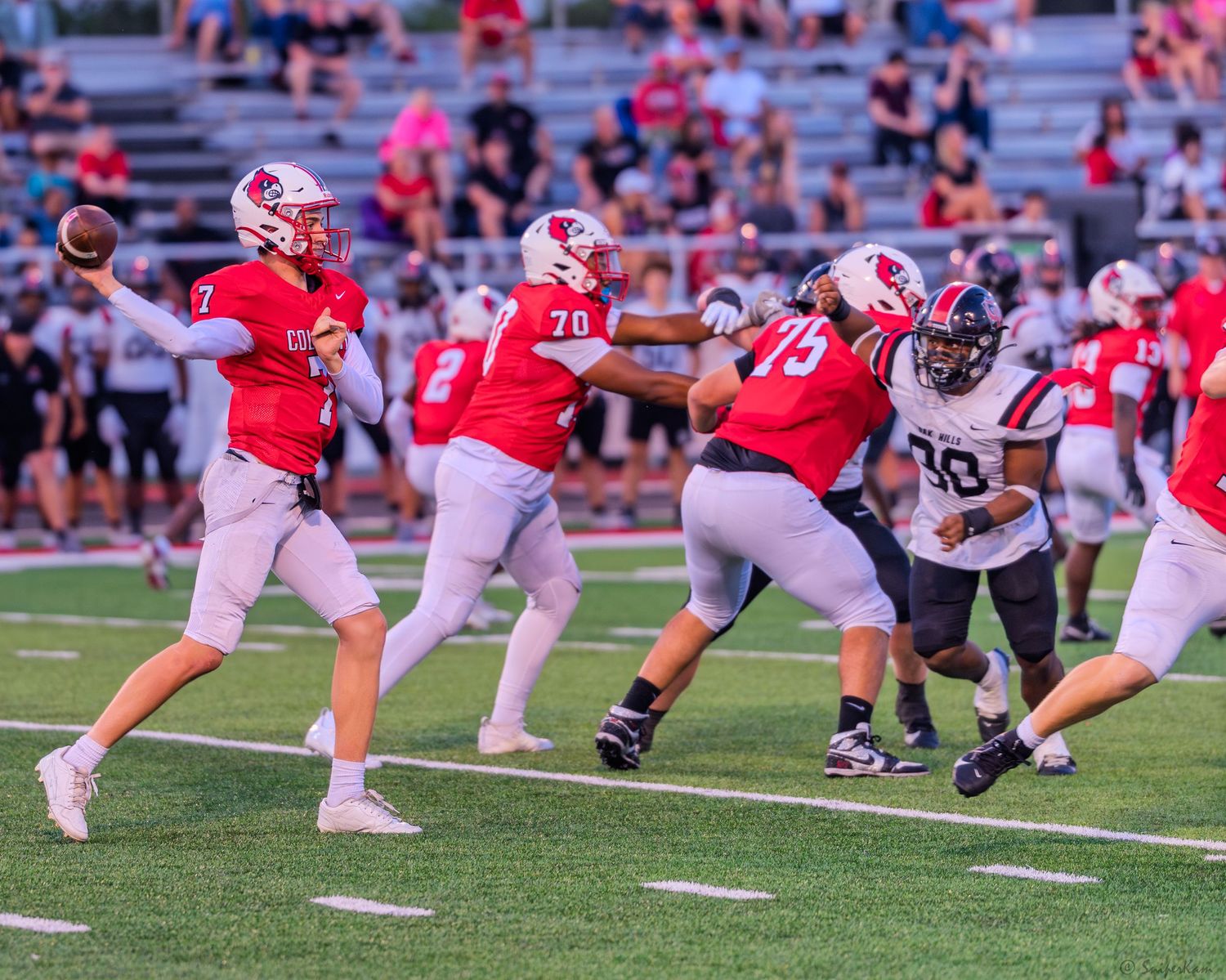 Colerain Cardinals quarterback number 7 throws a pass behind offensive line blocking during a night game.