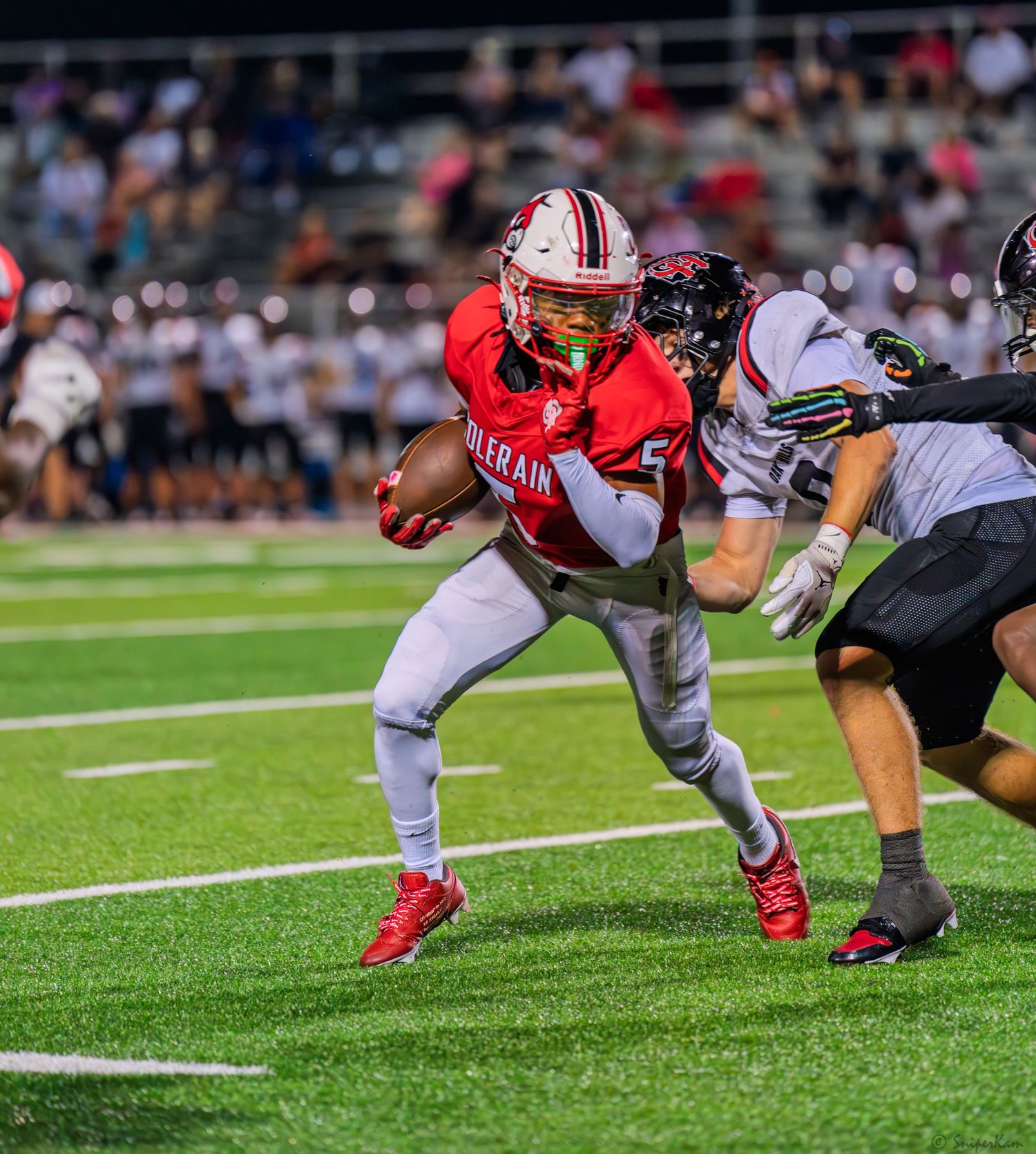 Colerain running back in red uniform breaks through a tackle attempt during a night football game.