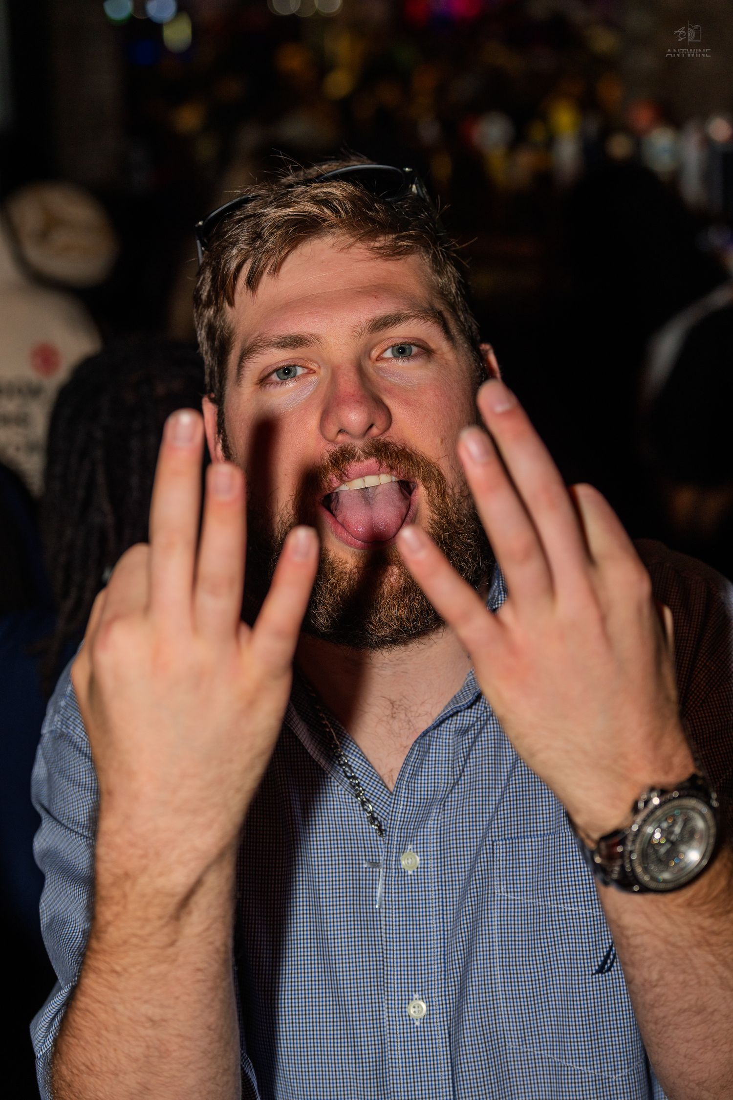 Bearded man making a funny face with hands spread wide and tongue out at a party.