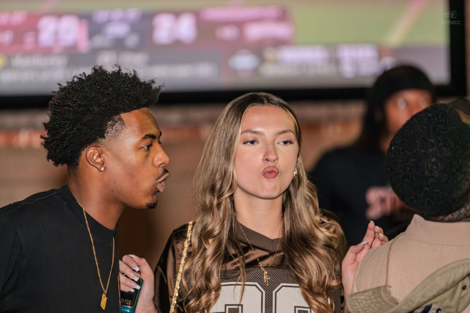 Young couple posing together at a sports bar with football game on big screen.