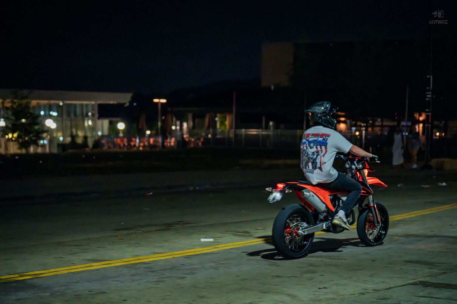 Motorcyclist riding a red dirt bike on a city street at night under bright lights.