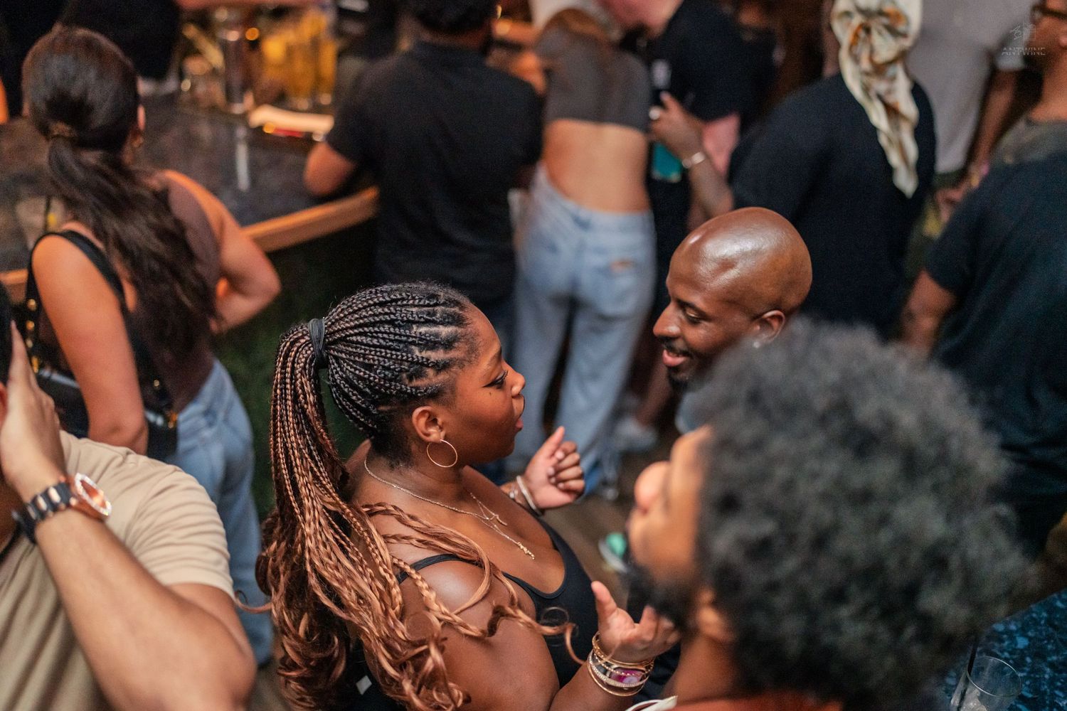 Bald man smiling and talking with woman wearing braids at a lively nightclub.