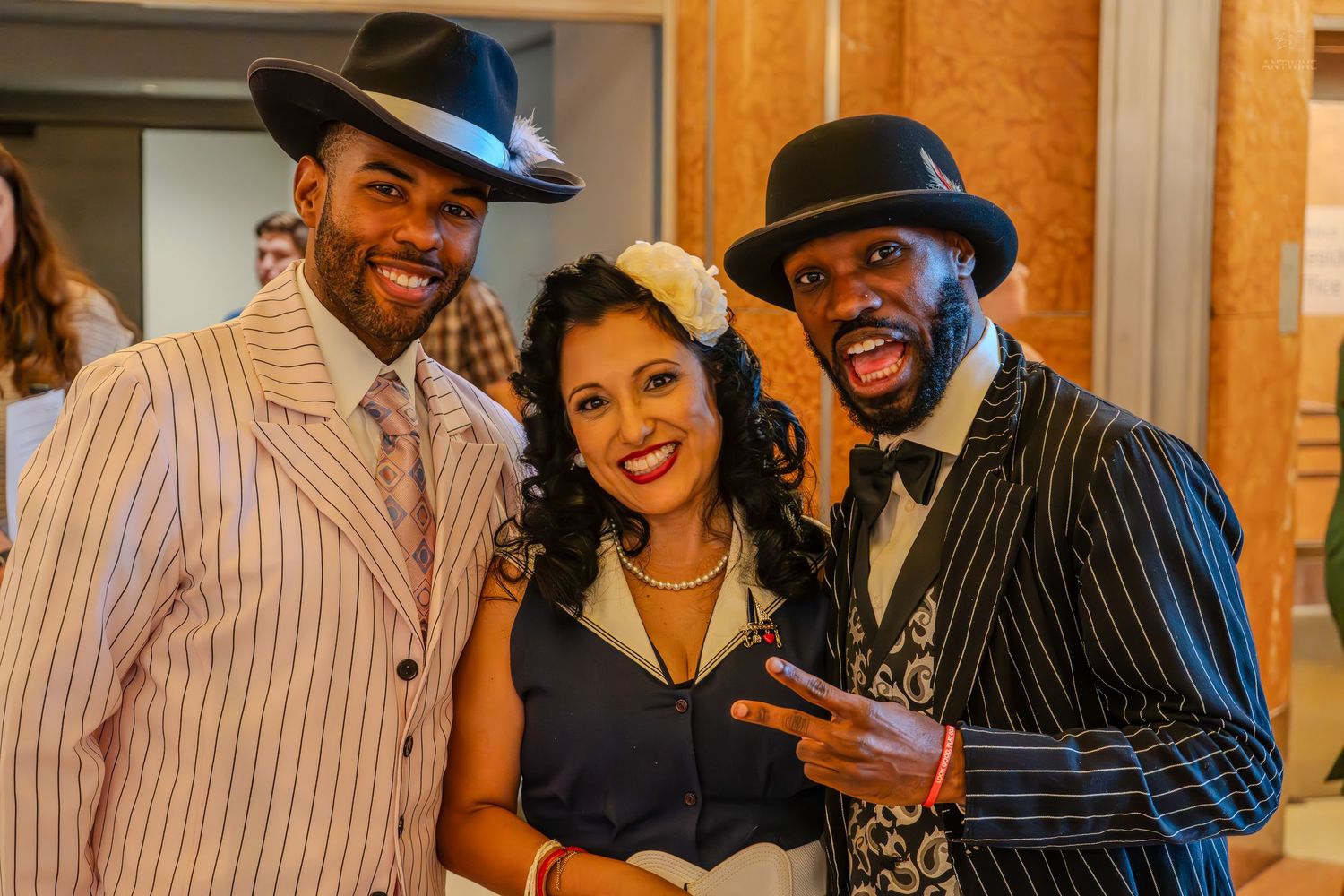 Three friends in vintage 1920s gangster-style outfits pose together, smiling at a retro-themed event.