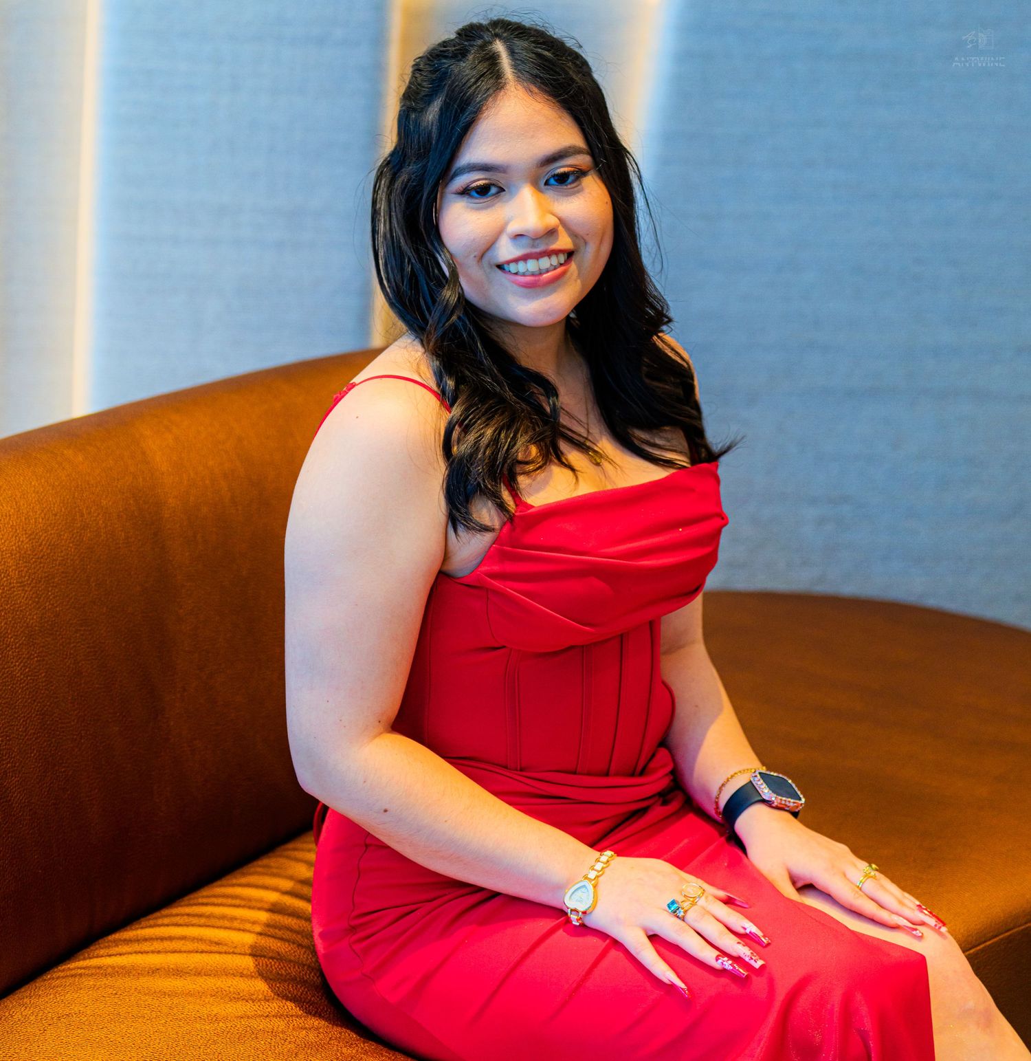 Woman in a red strapless dress smiling warmly while seated on a leather sofa in a stylish interior.