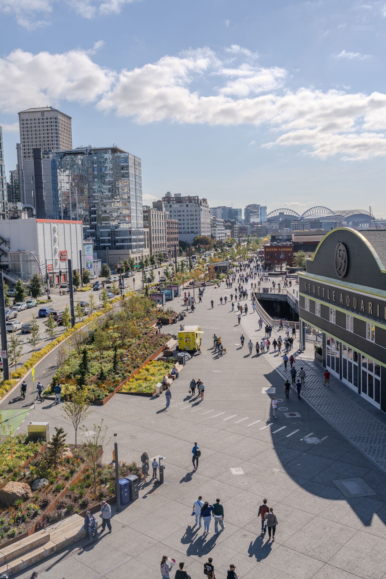 Aerial view of Seattle's waterfront plaza near Pike Place Market with crowds of people walking on a sunny day.