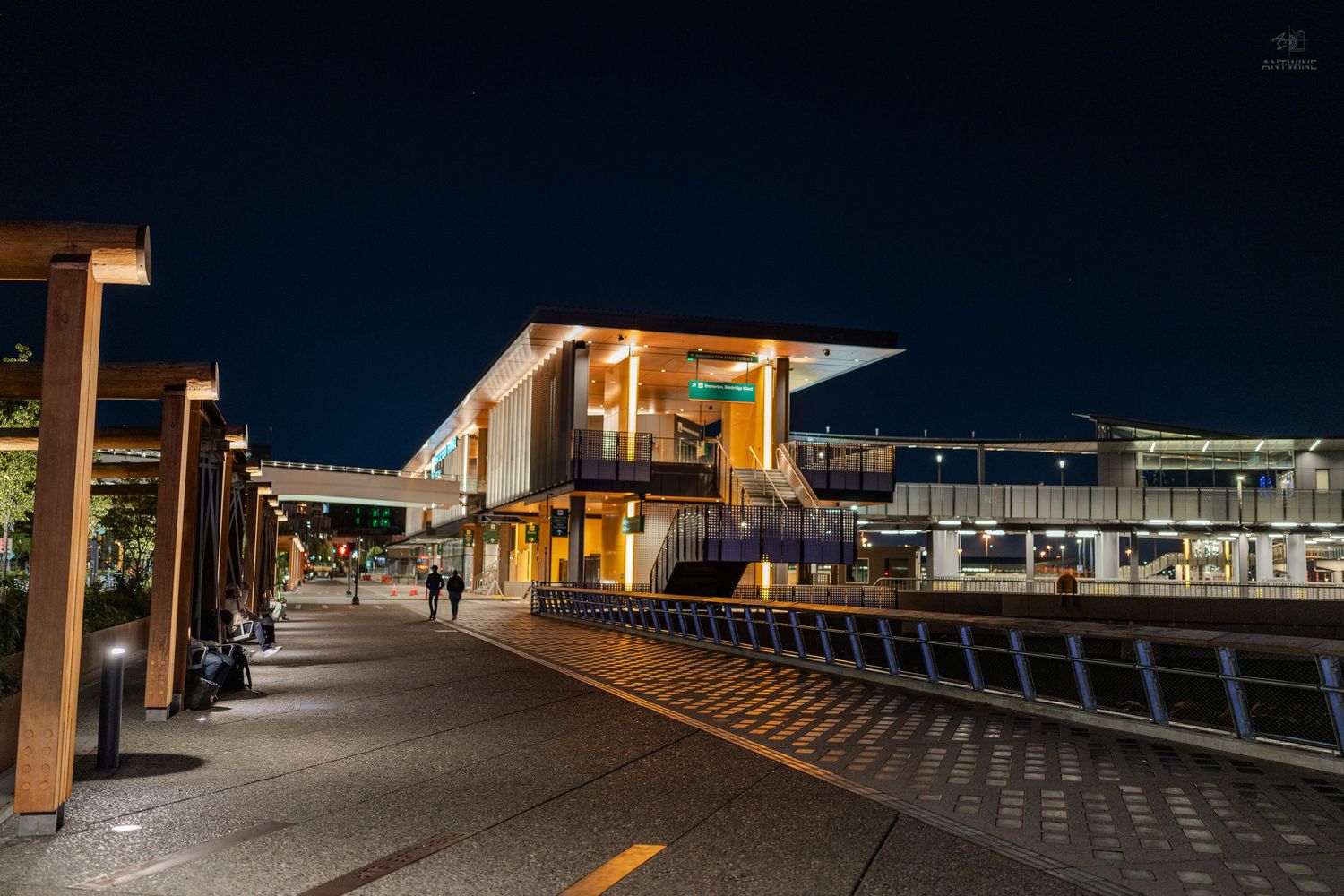 Modern transit station illuminated at night with warm lights reflecting on empty platforms under a clear dark sky.