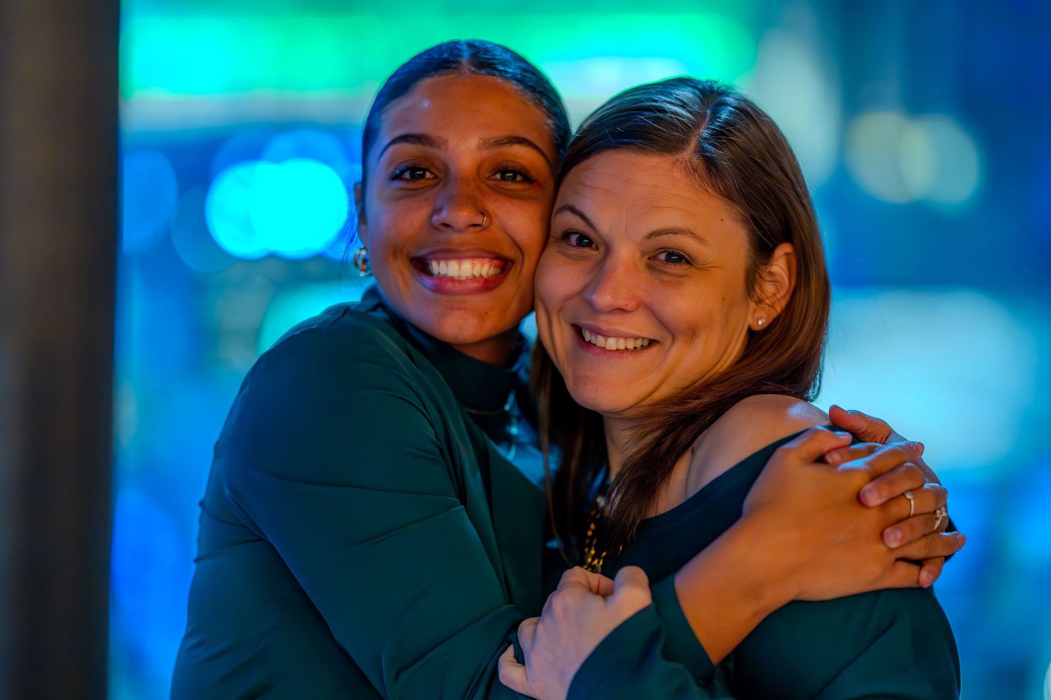 Two happy women embracing and smiling together in front of blue bokeh lights.