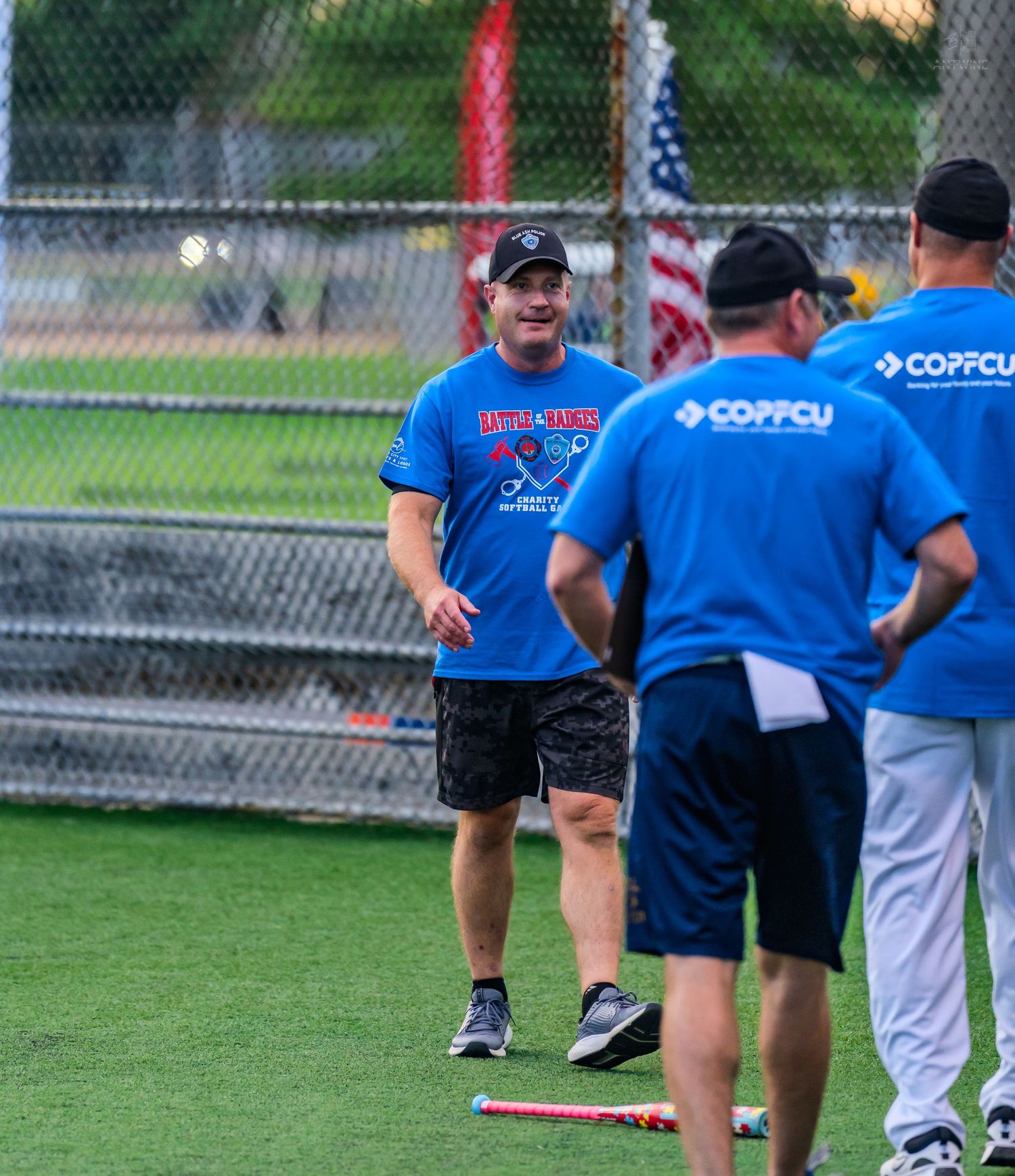 Softball players in blue and white jerseys chat on a green field during a recreational game.