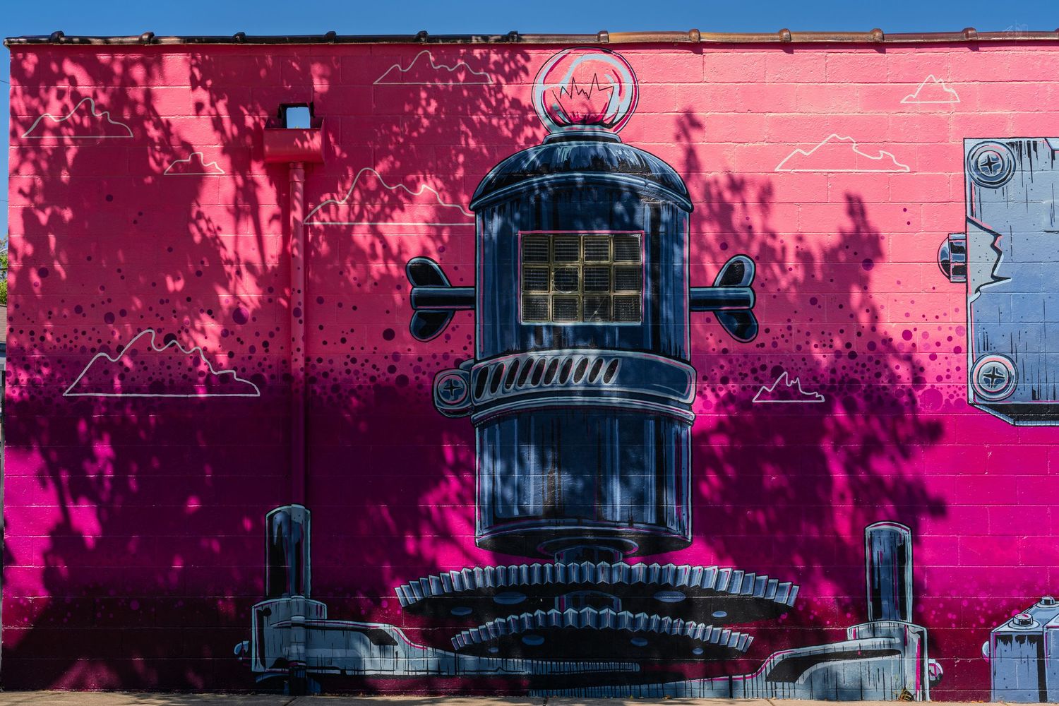 Vibrant pink mural on a building wall featuring a large industrial machine painted in black and gray street art style.