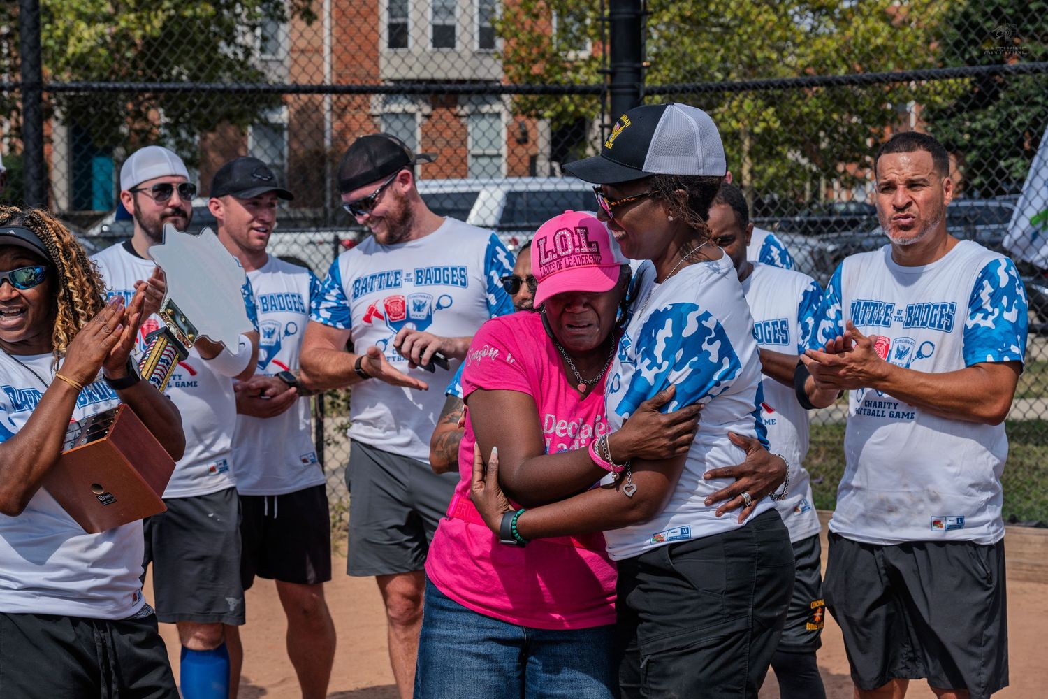 Charity softball players applaud and celebrate emotional moment with woman in pink shirt.