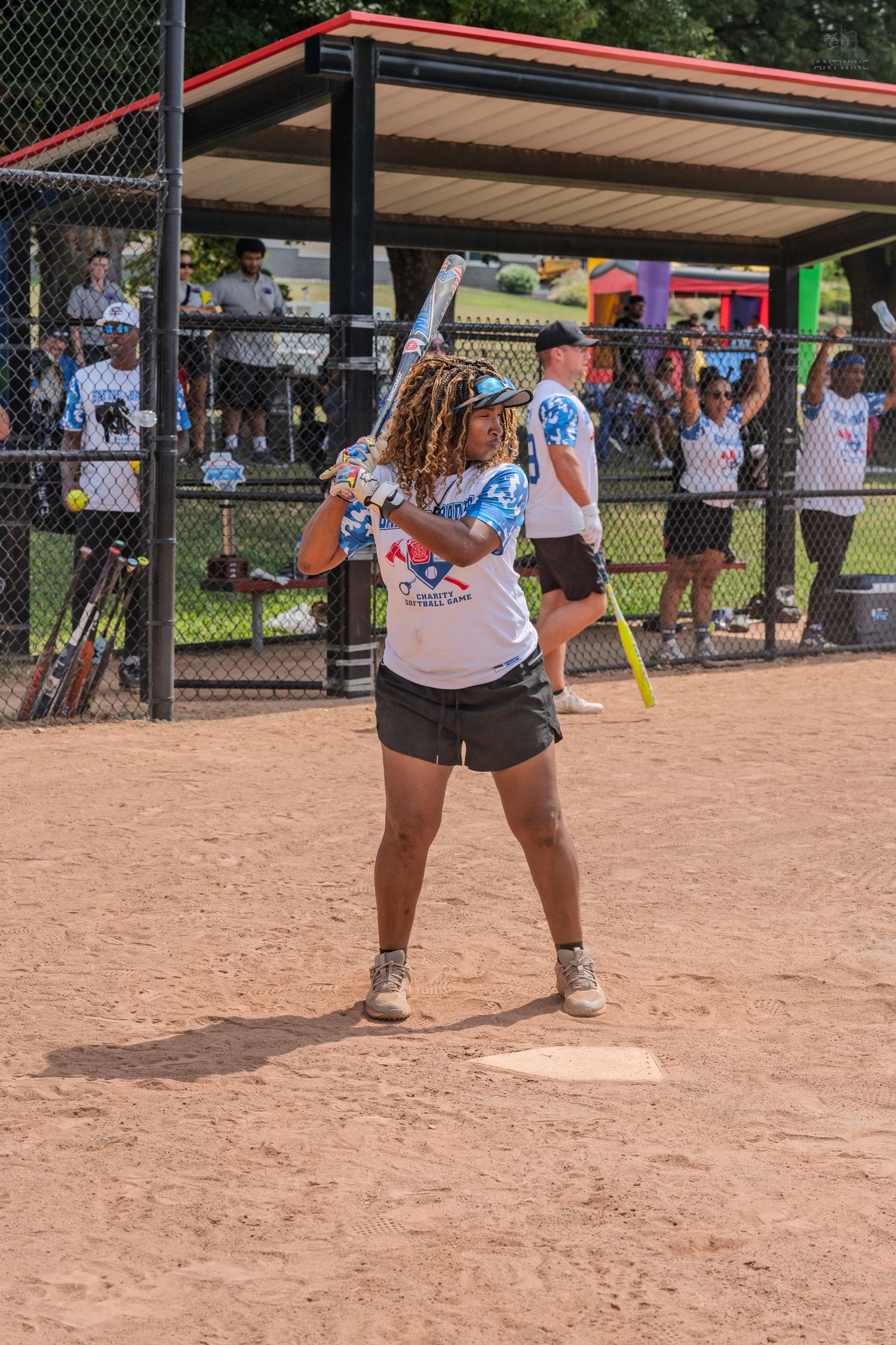 A woman with dreadlocks prepares to bat during a sunny outdoor softball game.