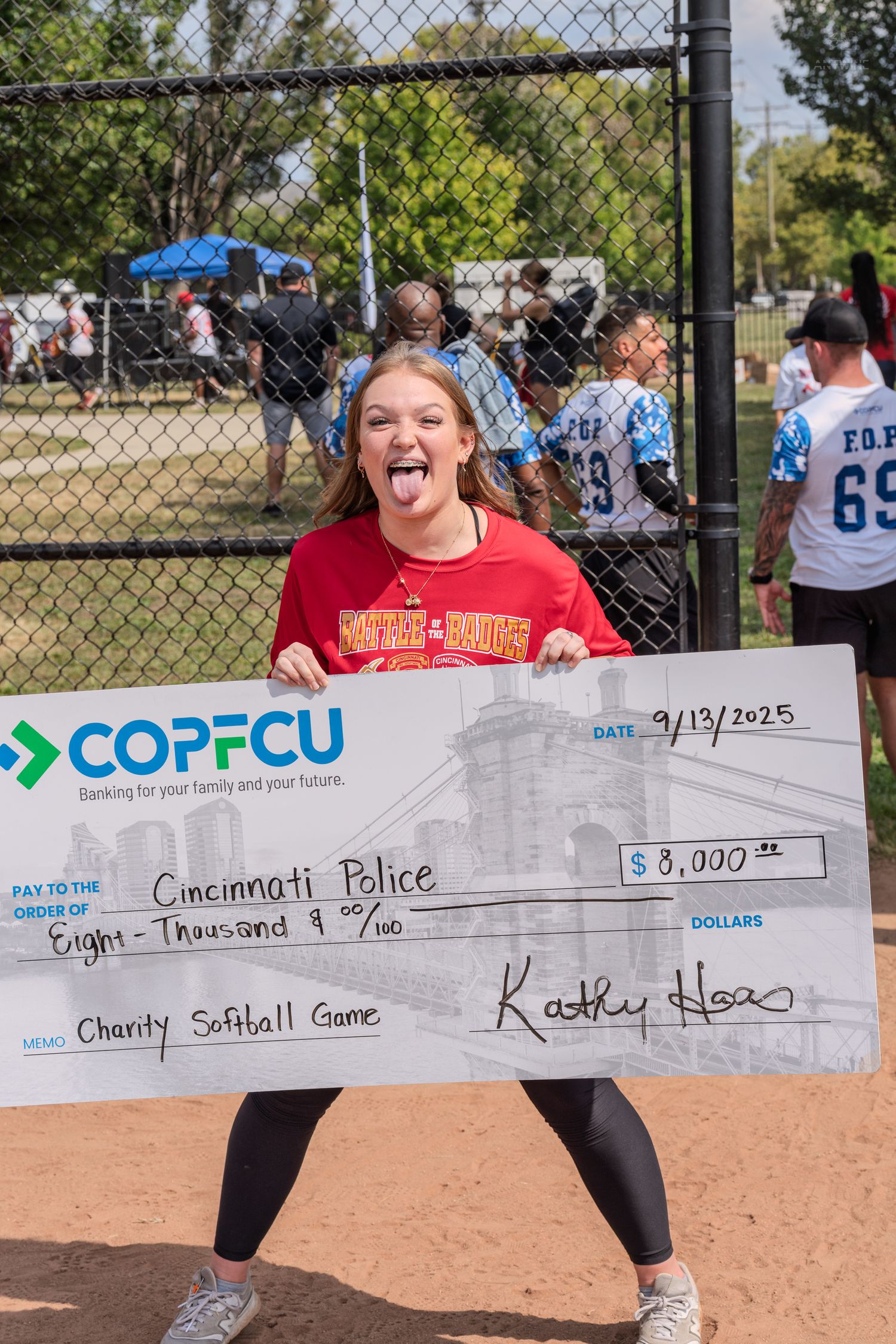Girl holds COPFCU $8,000 check payable to Cincinnati Police from a charity softball game dated 9/13/2025.